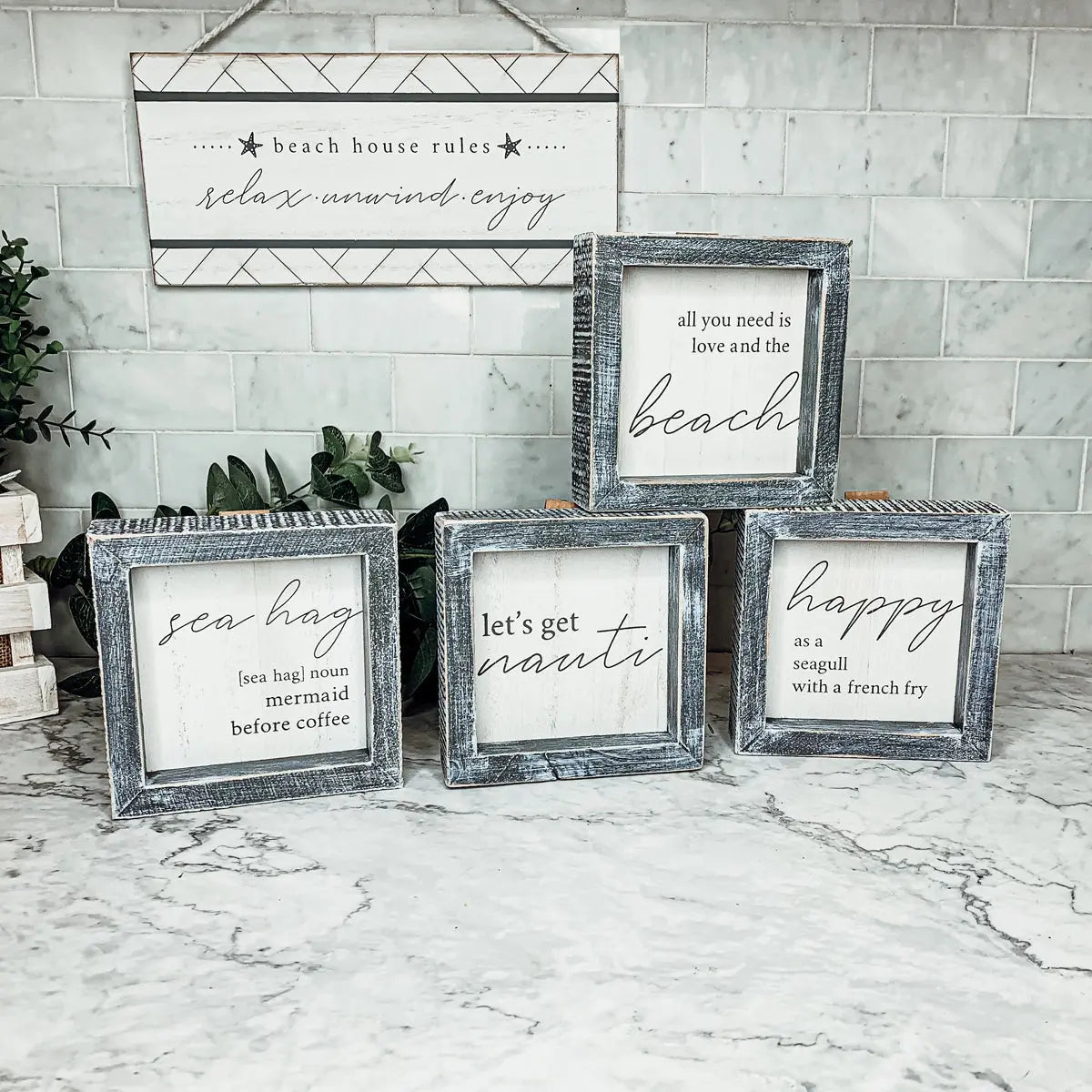 Set of framed beach-themed signs on a marble surface with a tiled wall background.