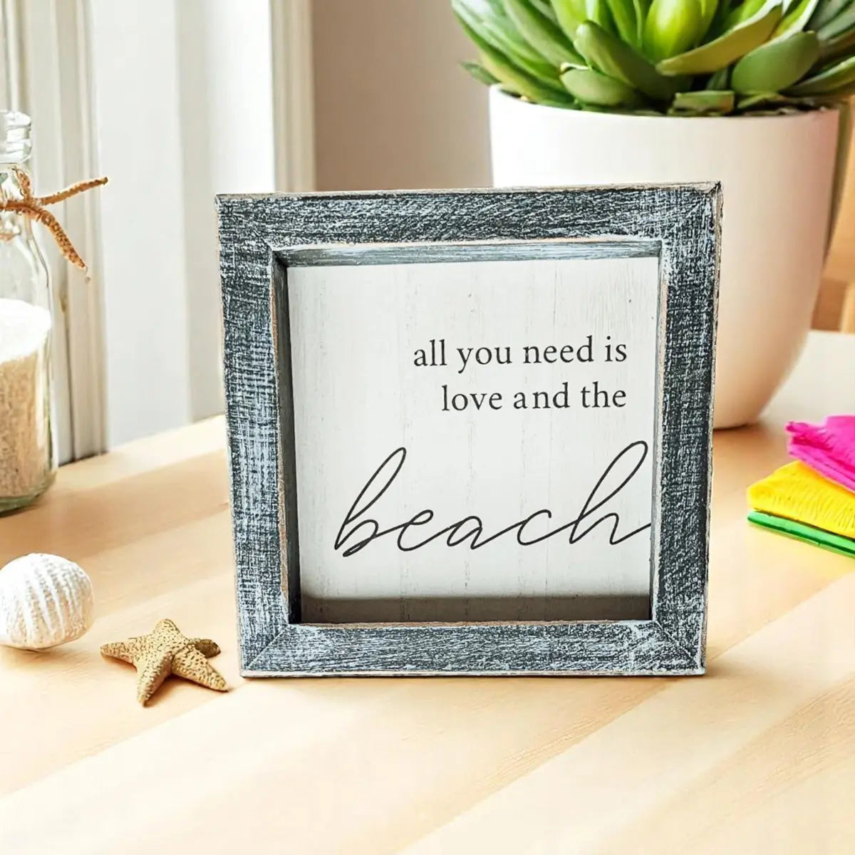 Decorative sign with 'all you need is love and the beach' text on a table with decorative items.