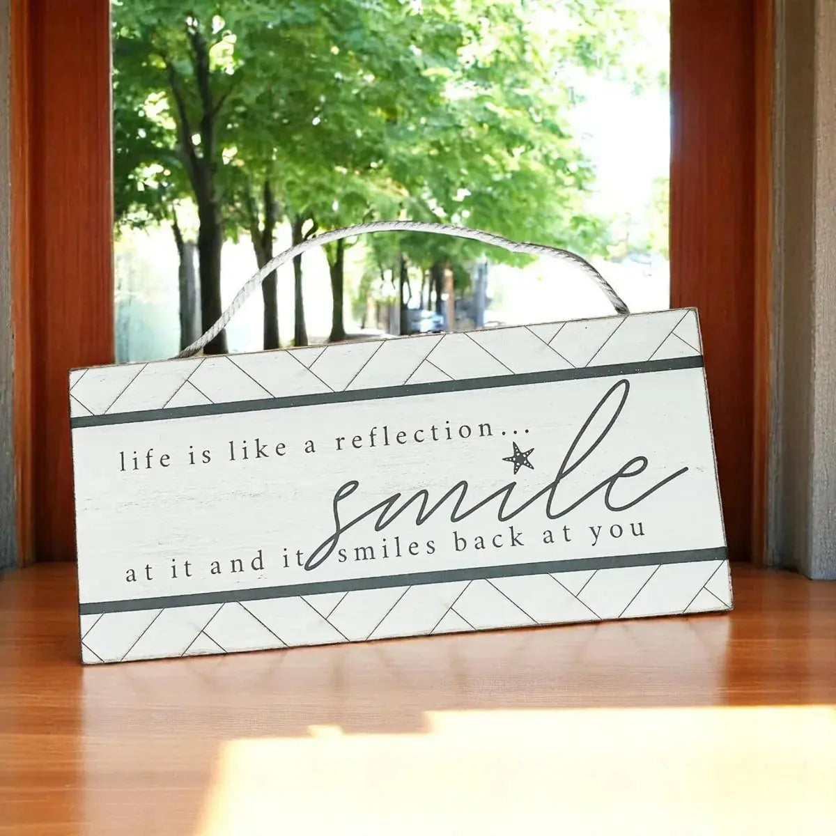 Decorative sign with motivational quote on a wooden floor, with a window in the background showing trees.