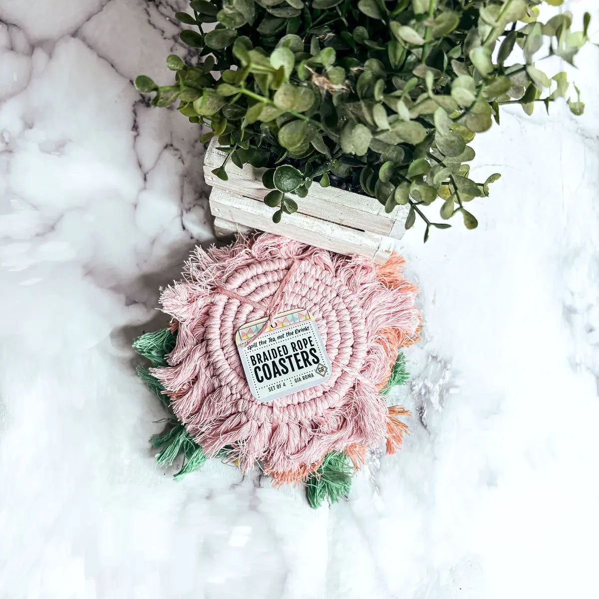 Pink braided rope coaster with a label on a marble surface with greenery
