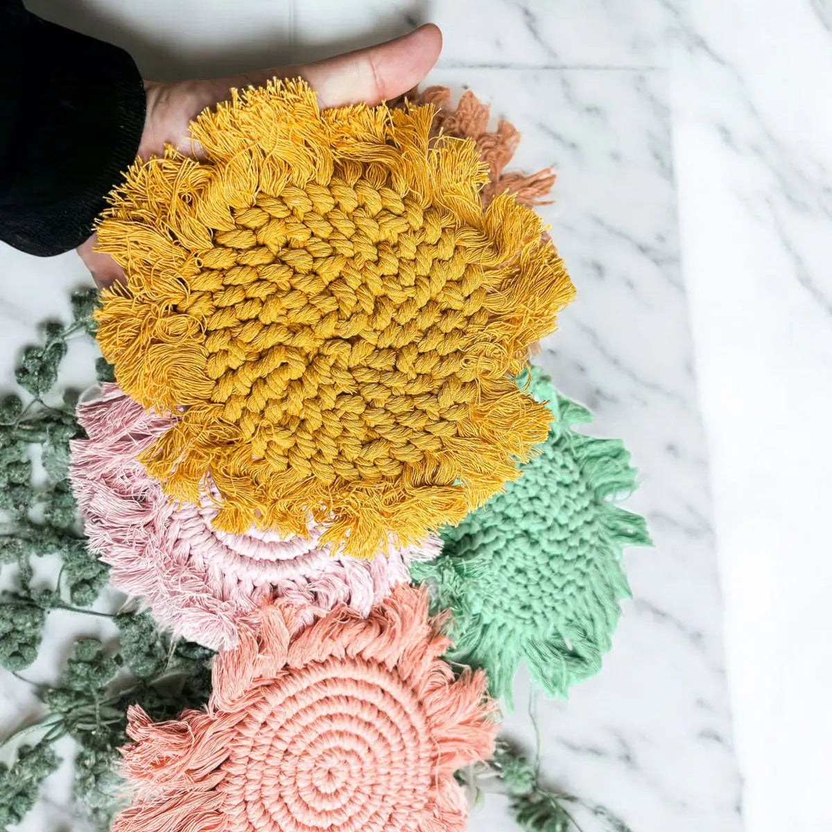 Hand holding a yellow textured round object with other colorful round objects on a marble surface.