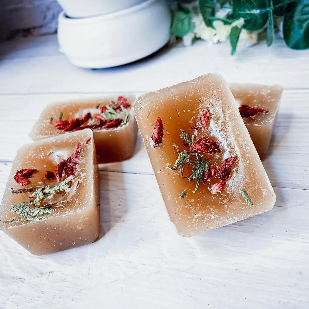 Four square soap bars with dried herbs on a white wooden surface