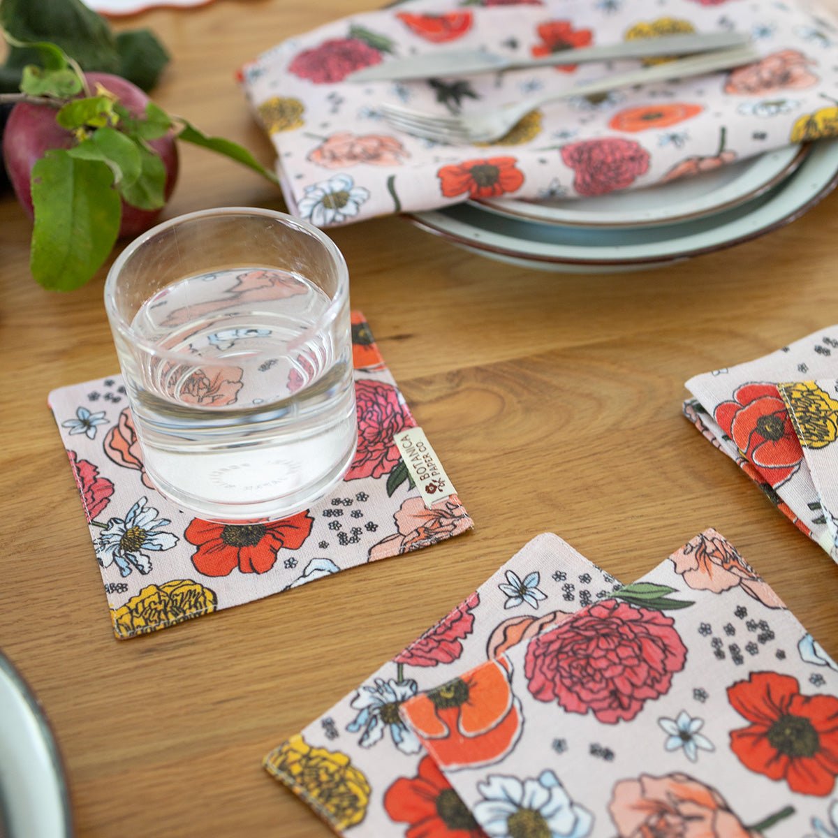 Floral-patterned coasters and napkins on a wooden table with a glass of water.