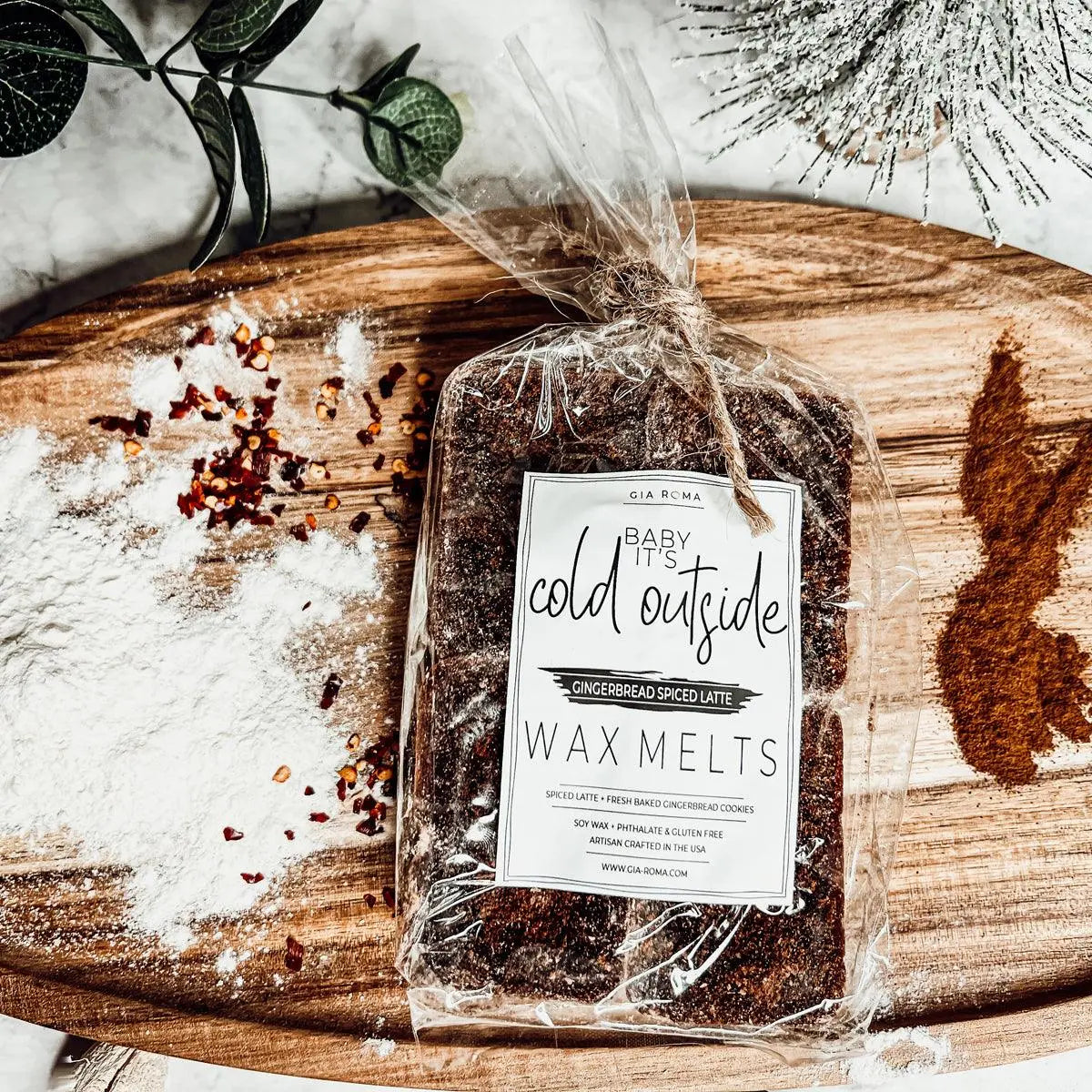 Packaged wax melts labeled 'Baby It's Cold Outside' on a wooden surface with decorative elements.