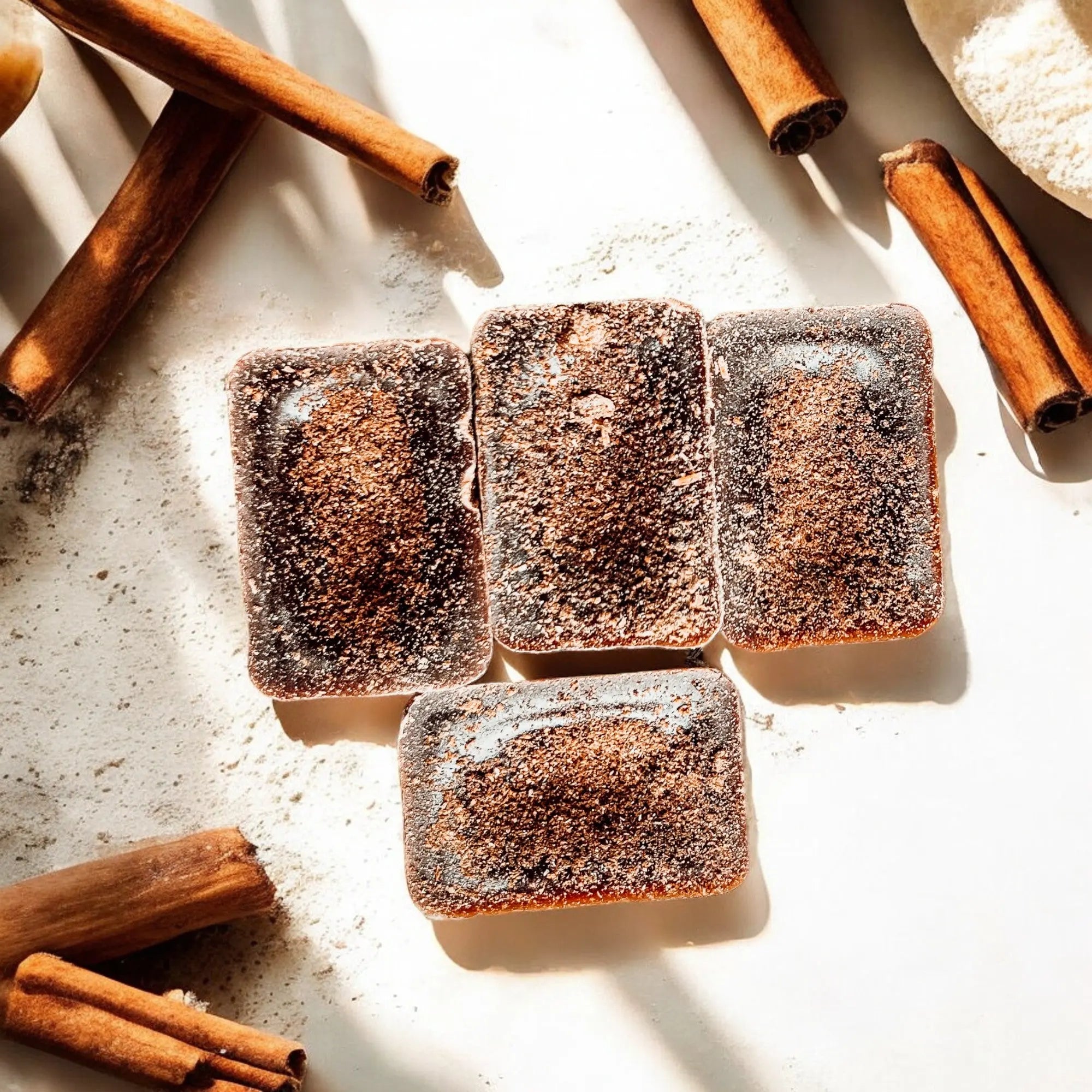 Square pastries dusted with cinnamon on a light surface with cinnamon sticks around