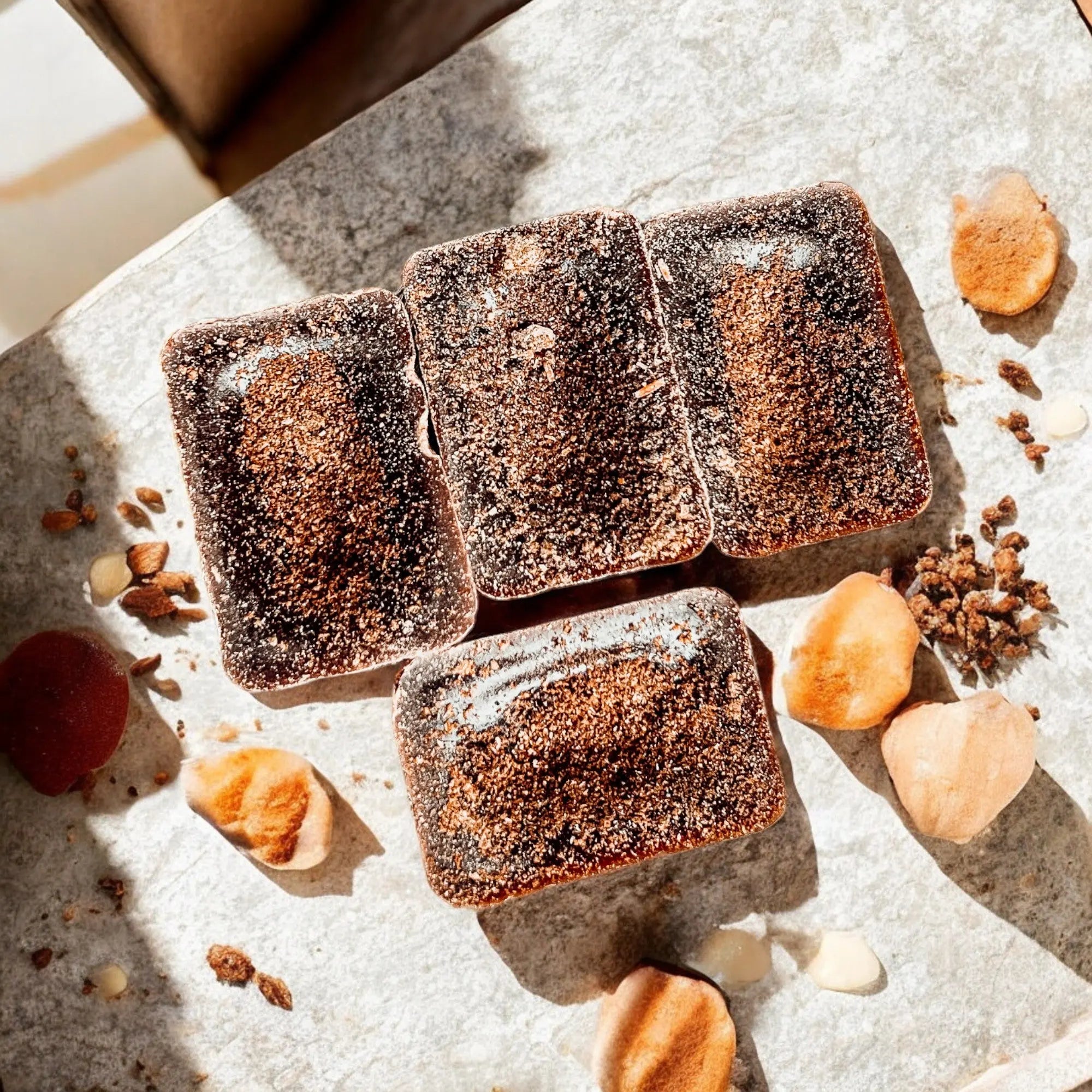 Square brownies with a dusting of cocoa powder on a textured surface with nuts and berries.