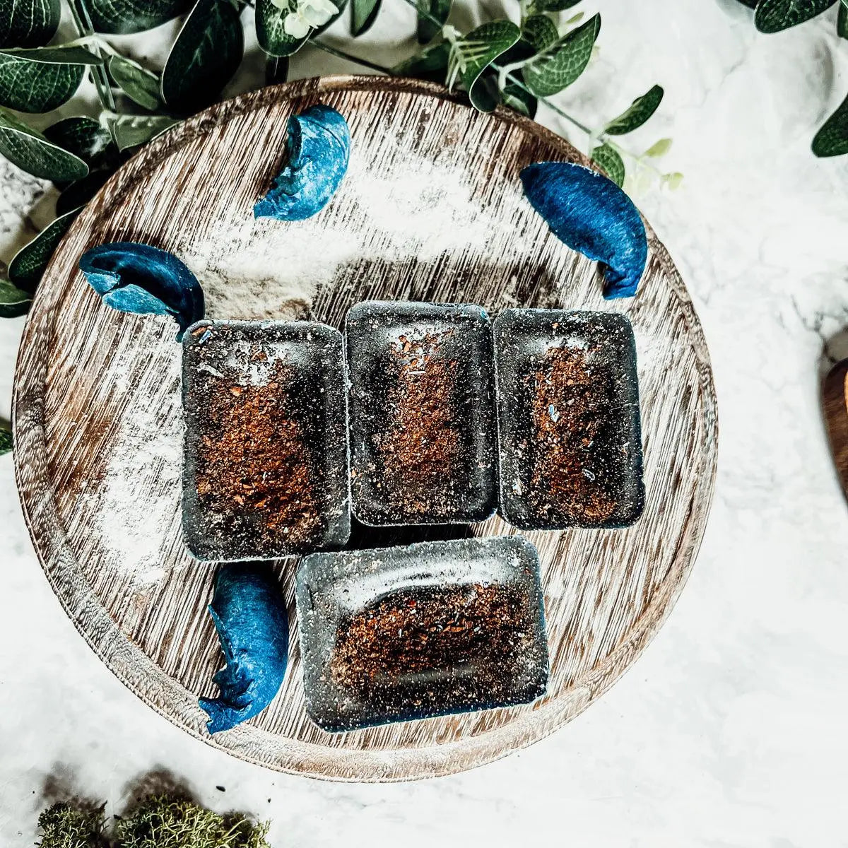 Wooden plate with dark brown rectangular items and blue leaves on a white background