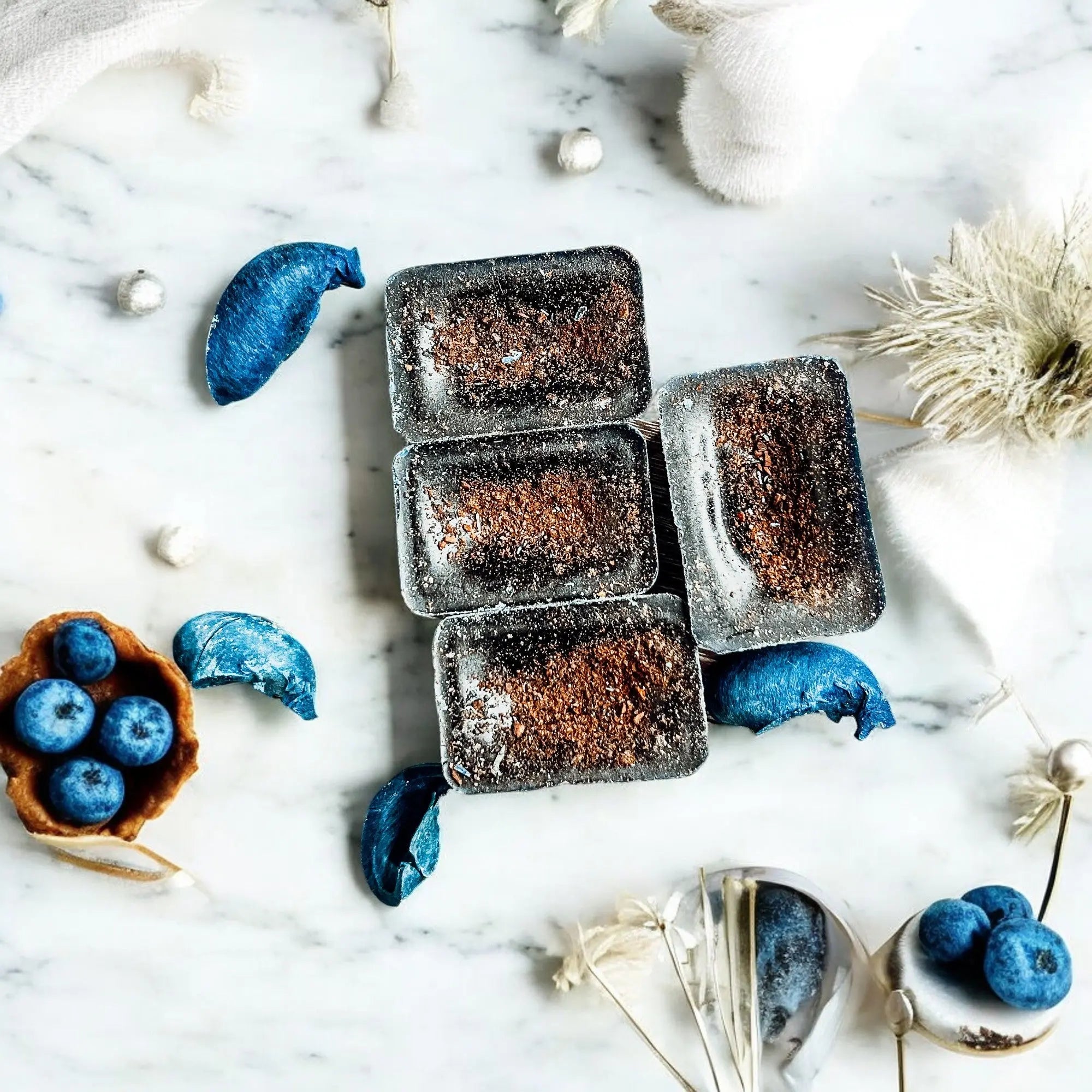Brownies in ice cube trays on a marble surface with blueberries and flowers.