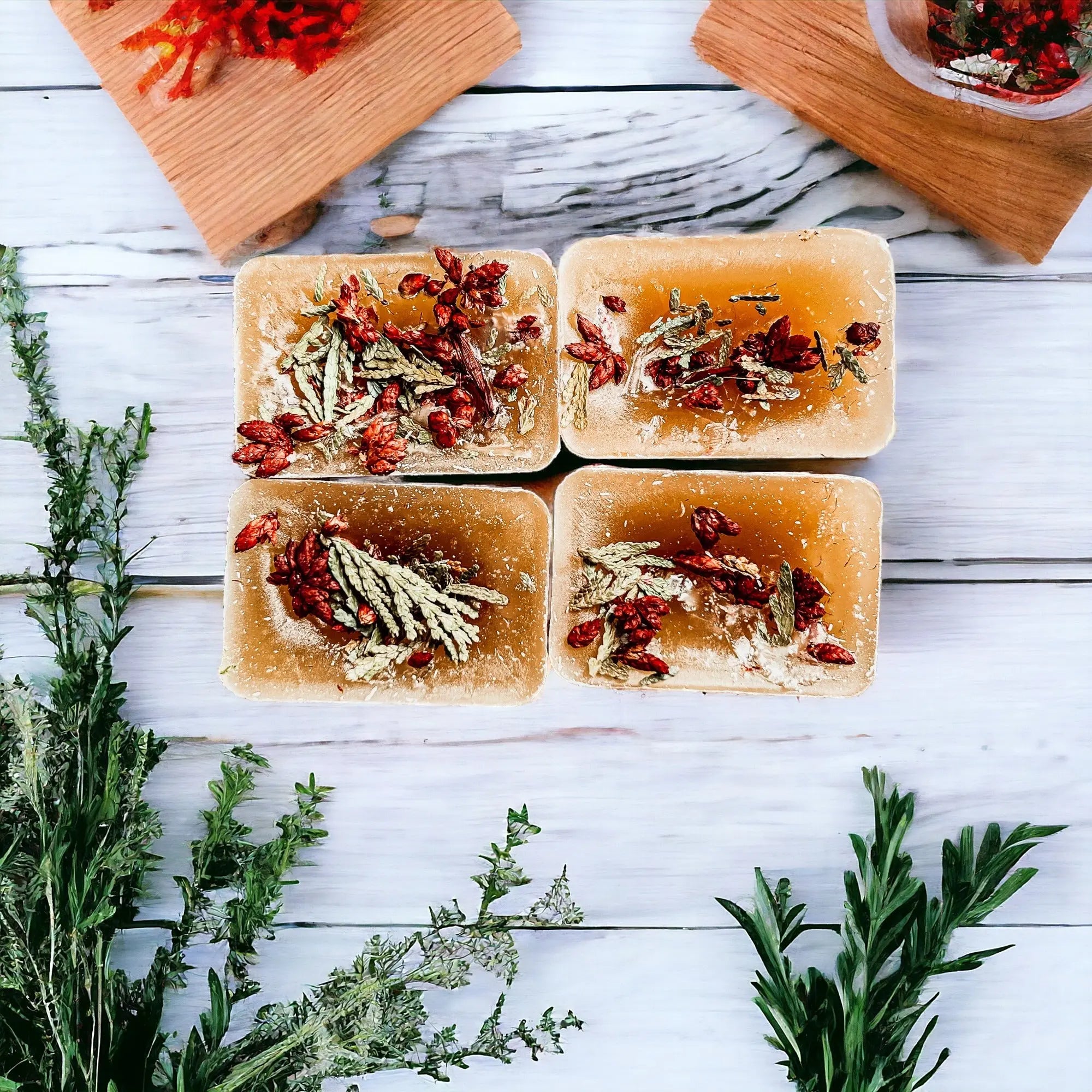 Four rectangular soap bars with natural ingredients on a wooden surface with herbs around.