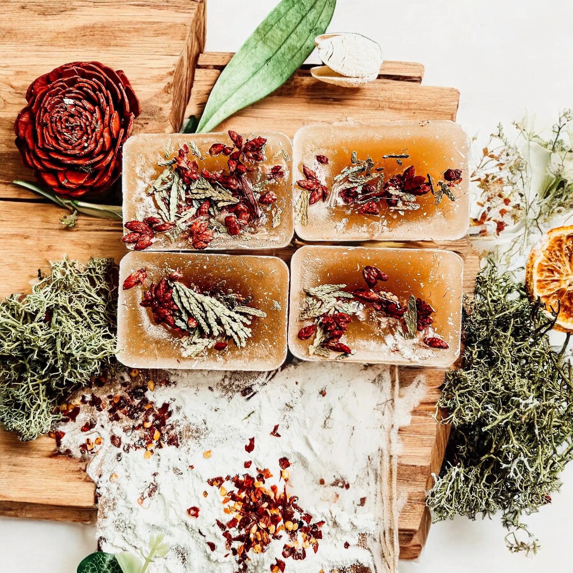 Four square soap bars with natural ingredients on a wooden board with decorative elements.