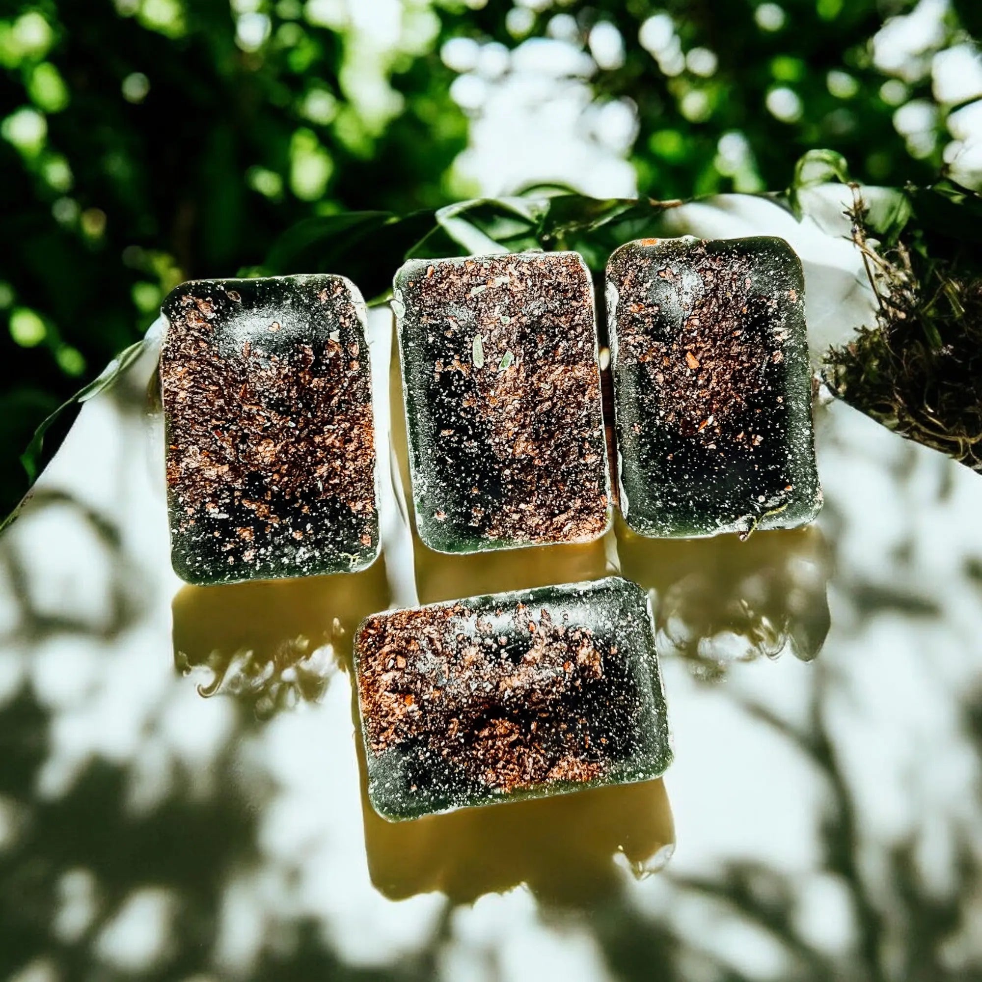 Four rectangular ice cubes with a dark brownish surface on a white cloth against a blurred green natural background.