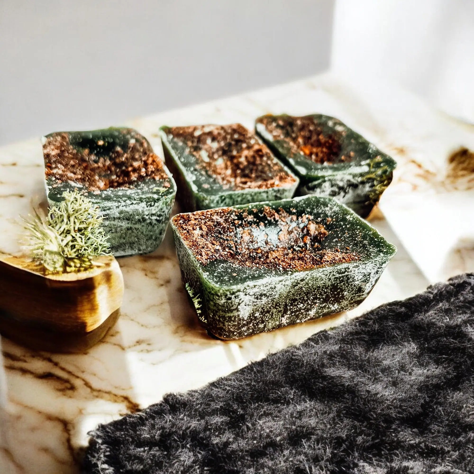 Green and brown soap bars on a marble surface with a wooden soap dish.