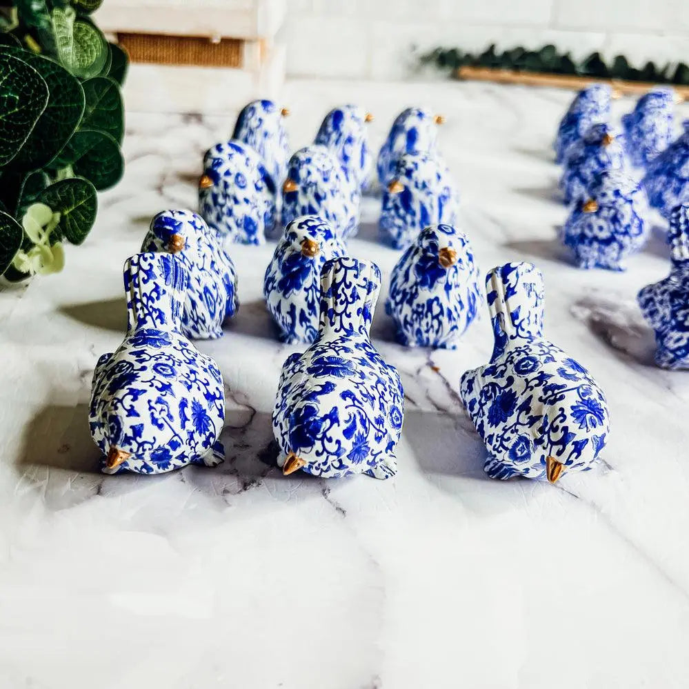 Blue and white ceramic birds on a marble surface with a plant in the background