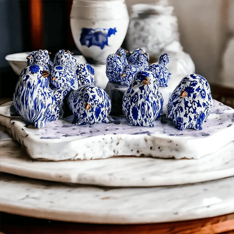 Blue and white ceramic birds on a marble surface with decorative vases in the background.