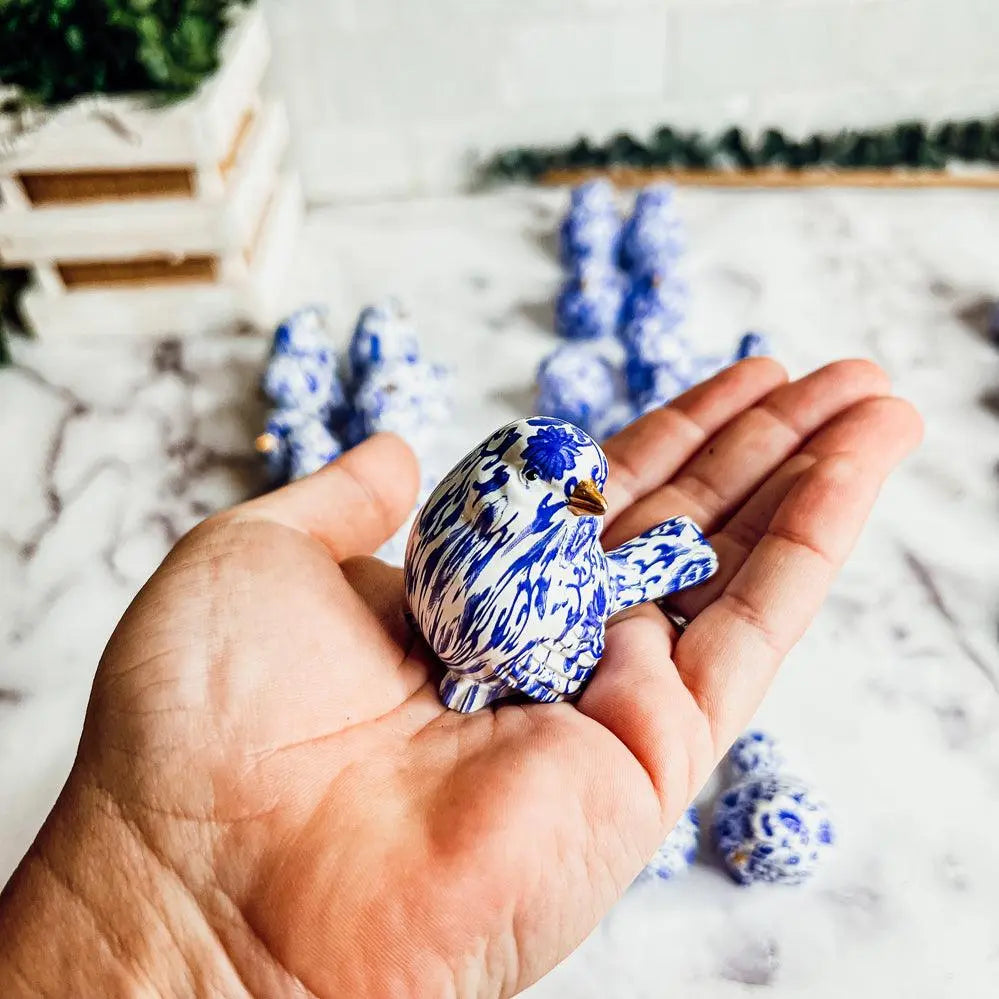 Hand holding a blue and white ceramic bird with more birds in the background on a light surface.