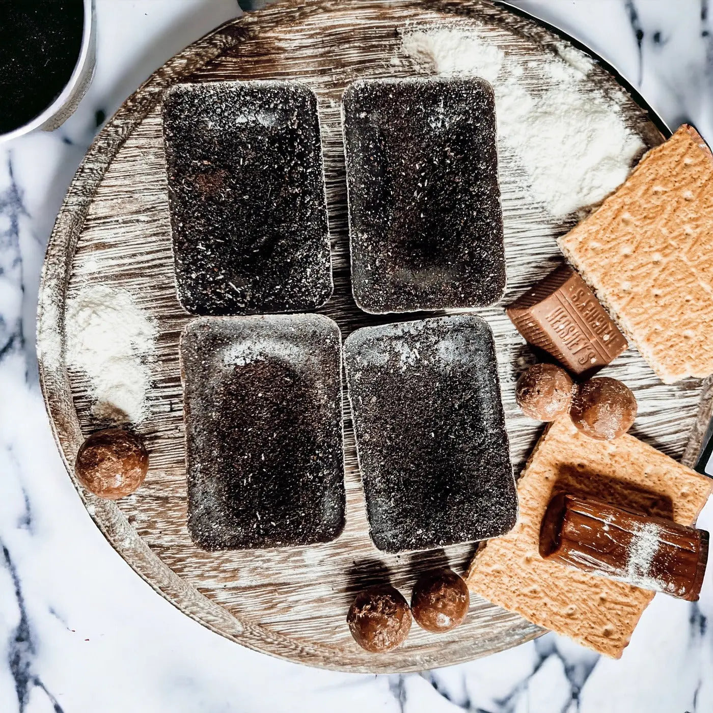 Dark chocolate bars and caramel squares on a wooden board with a marble background