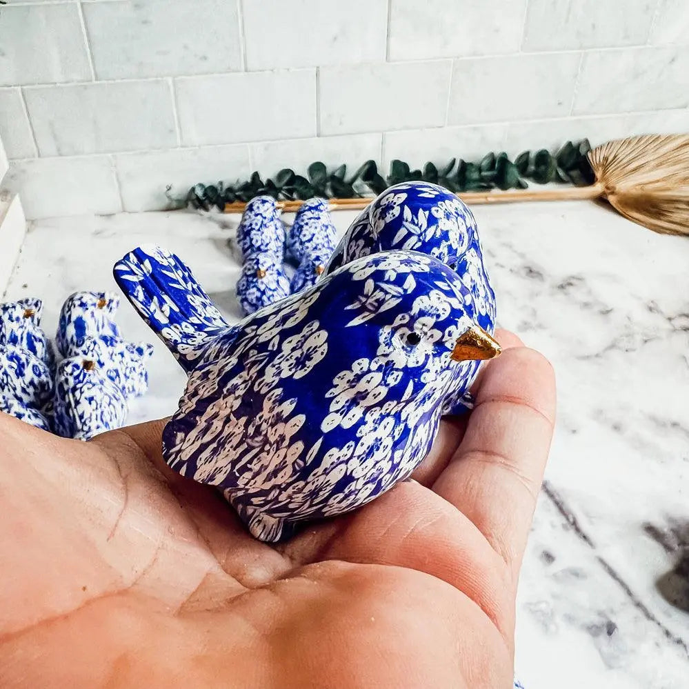 Blue and white ceramic bird-shaped object held in a hand with a marble background