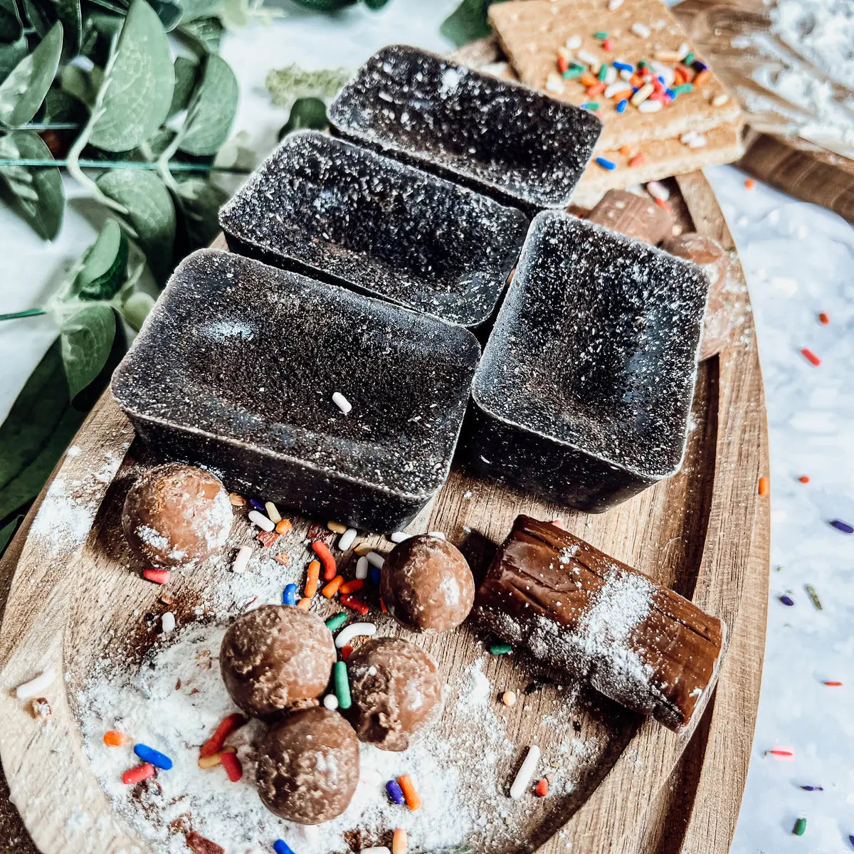 Dark chocolate truffles on a wooden board with powdered sugar and sprinkles.