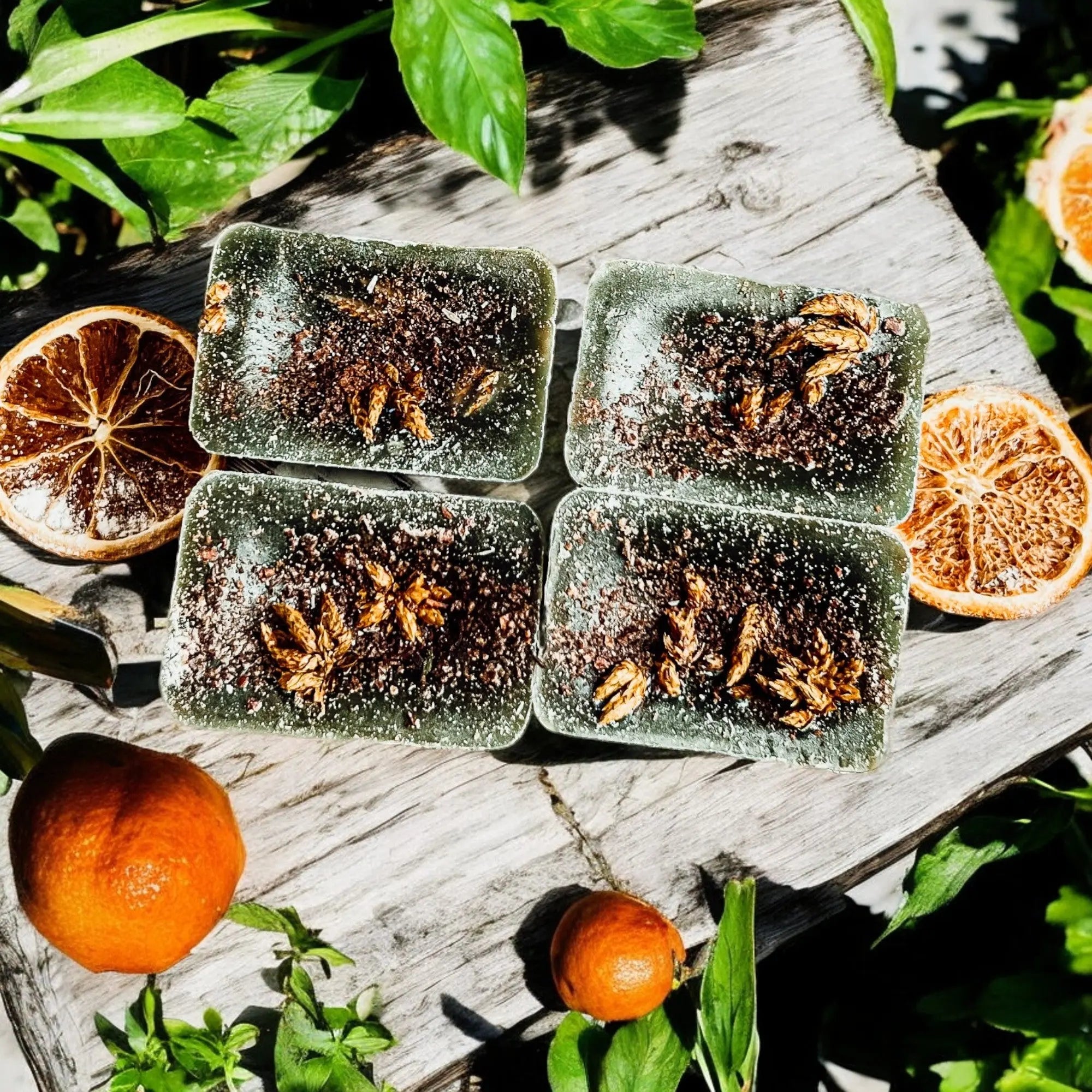 Four green soap bars with natural ingredients on a wooden surface with oranges and leaves.