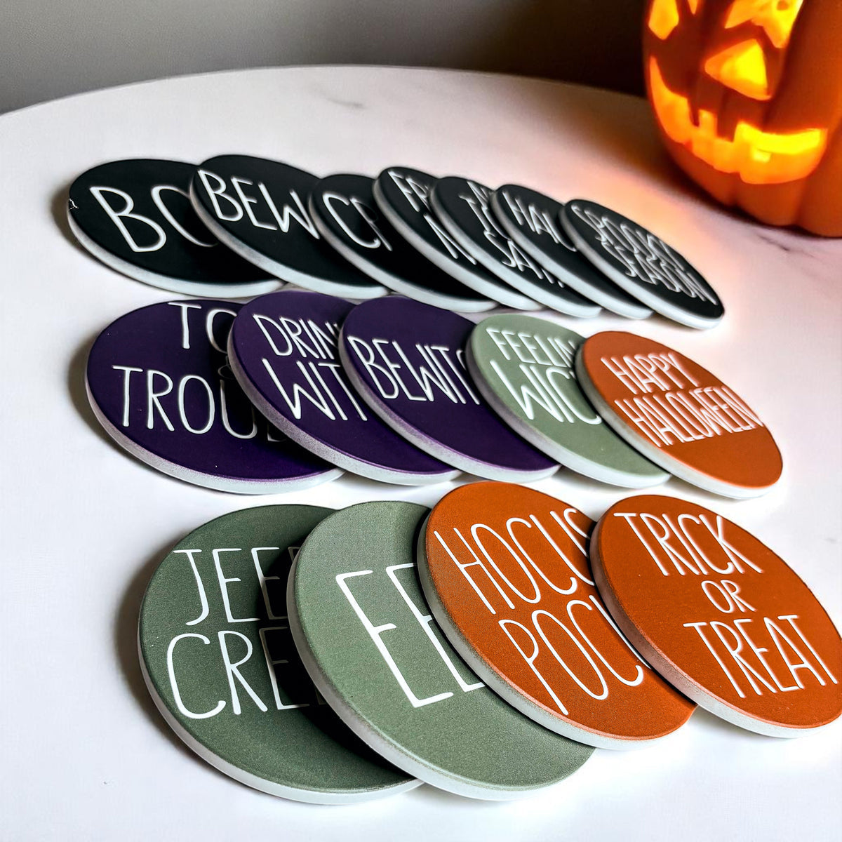 Set of Halloween-themed coasters on a white surface with a pumpkin in the background.