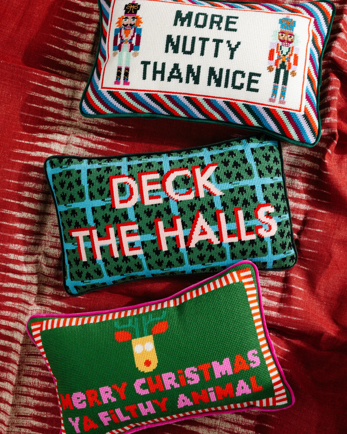 Three Christmas-themed needlepoint pillows on a red fabric background.