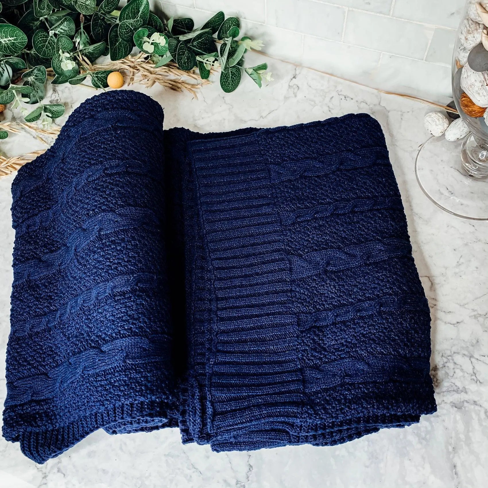 Navy blue cable knit throw blanket on marble surface with greenery decor
