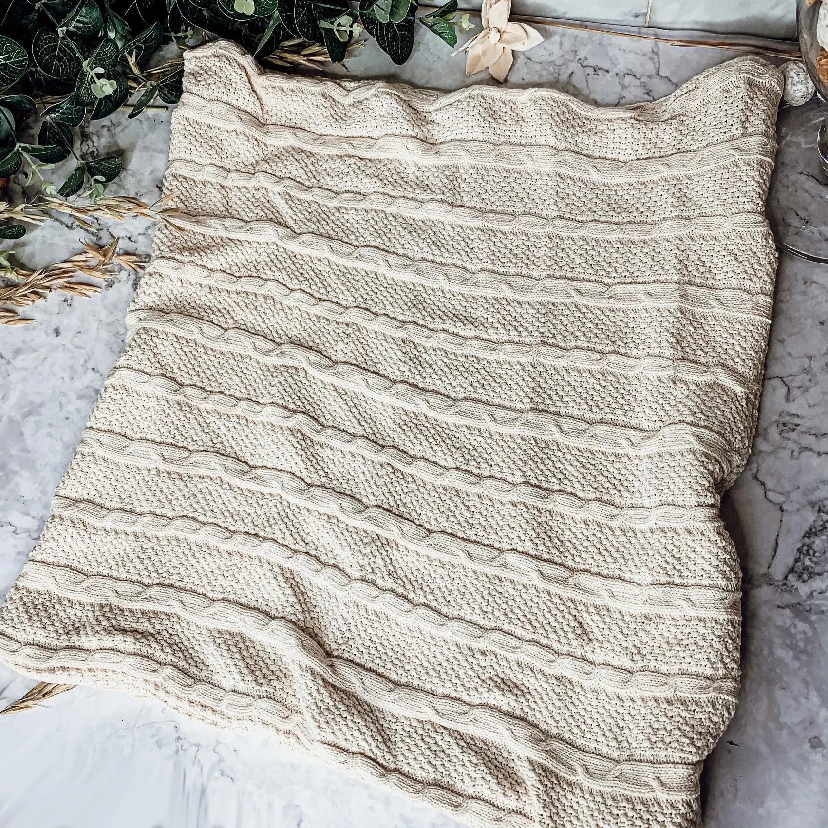 Cozy cream cable knit blanket on marble with greenery, perfect for farmhouse decor