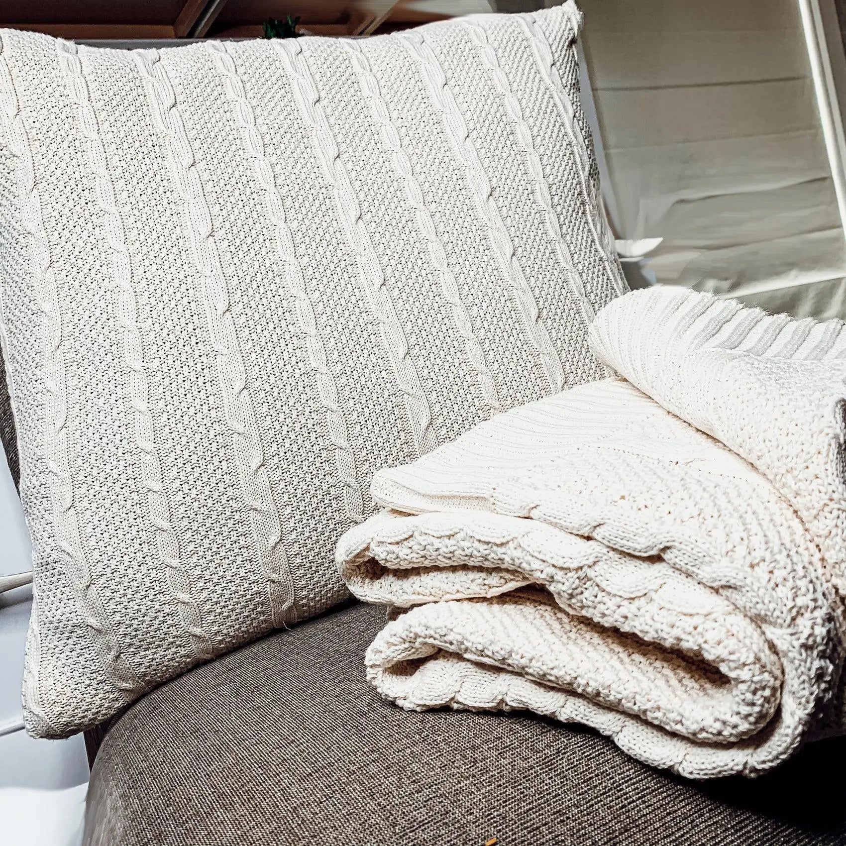 Cozy cream cable knit pillow and blanket on gray chair for farmhouse decor