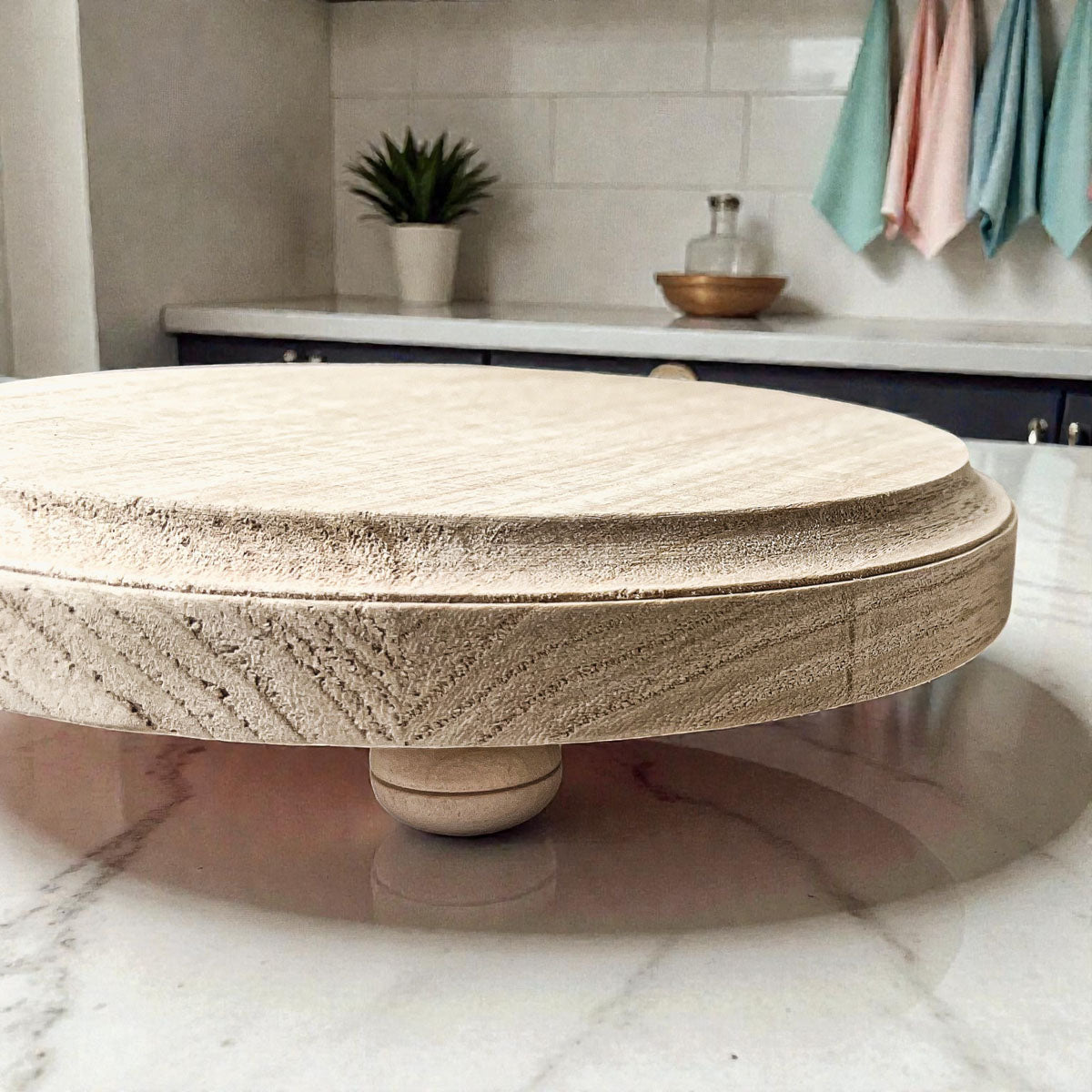 Round stone table in a kitchen setting with a plant and towels in the background.