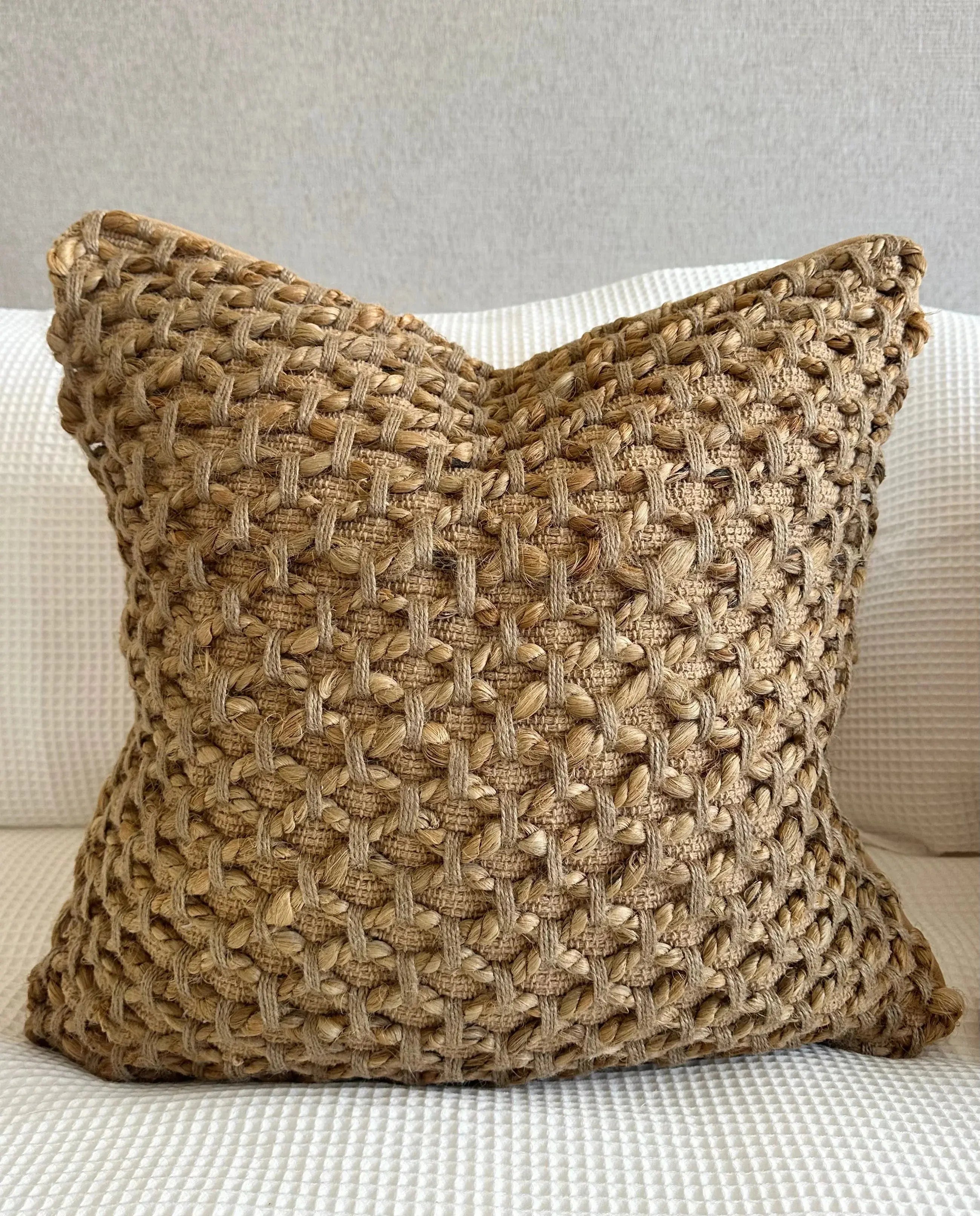 Woven jute throw pillow for cozy farmhouse decor on a white textured sofa