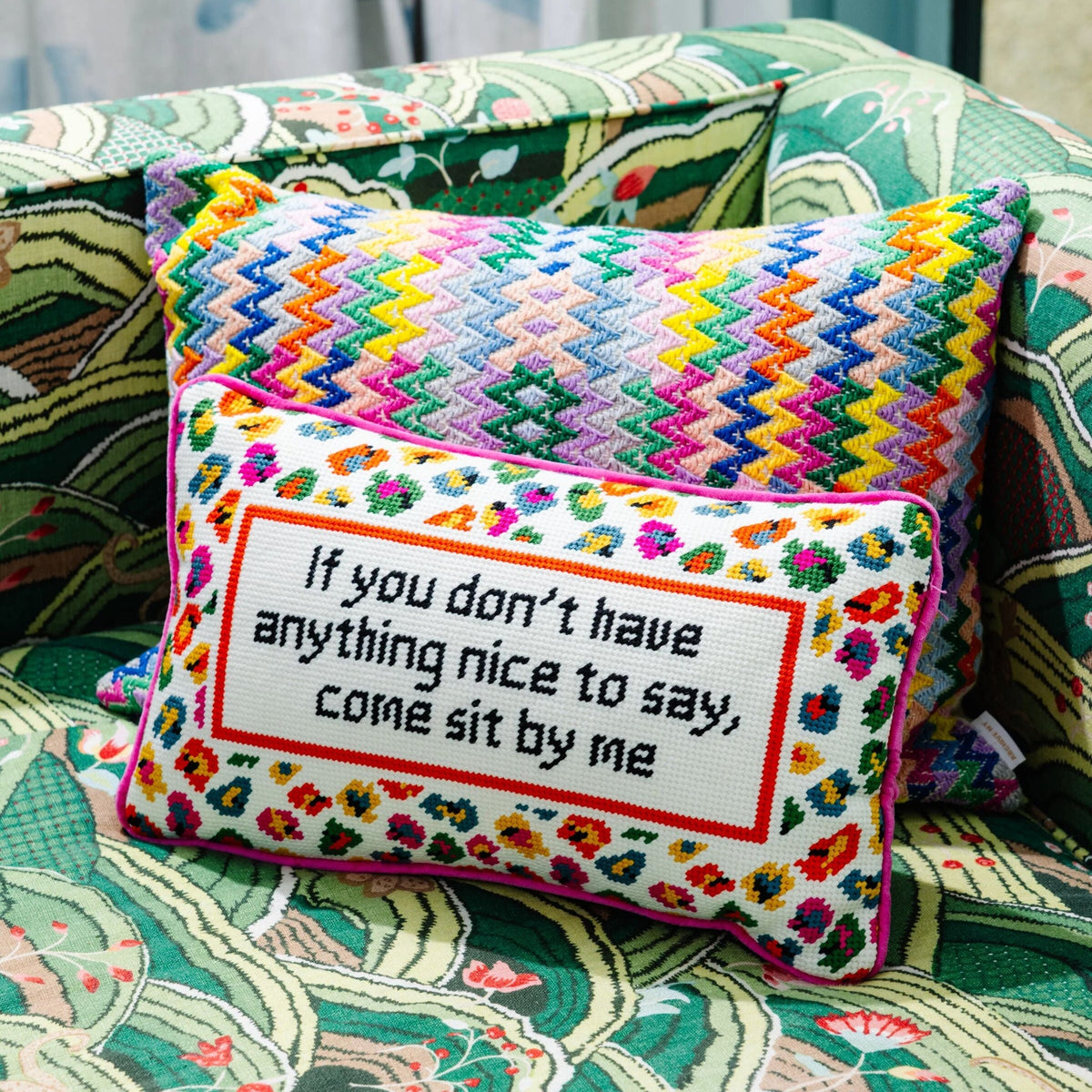 Colorful embroidered pillow with text on a patterned couch