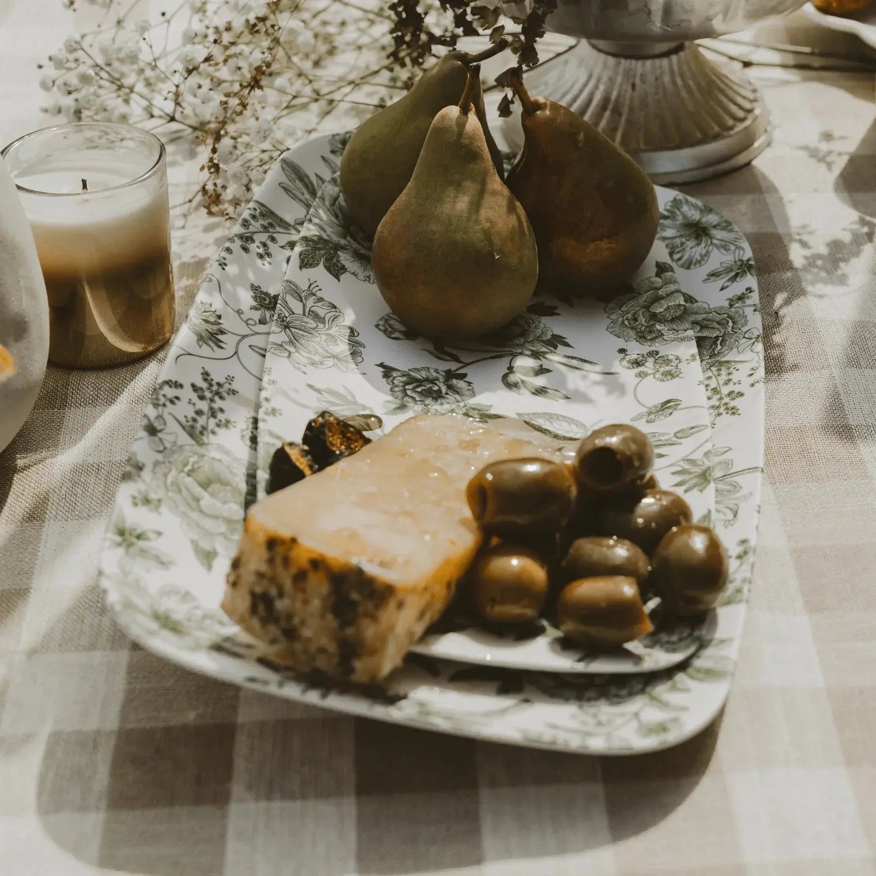 Farmhouse-style charcuterie tray with pears, cheese, olives, and candle on floral platter, cozy cottage decor