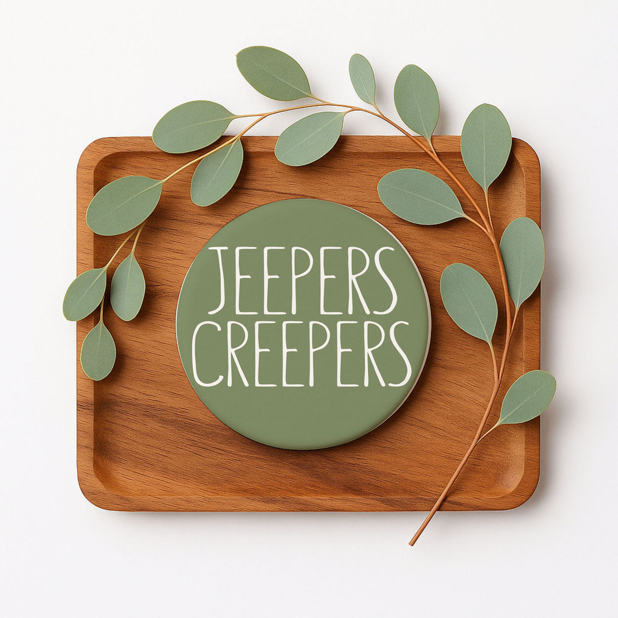 Wooden tray with a green circular sign reading 'Jeeper's Creepers' and decorative leaves on a white background