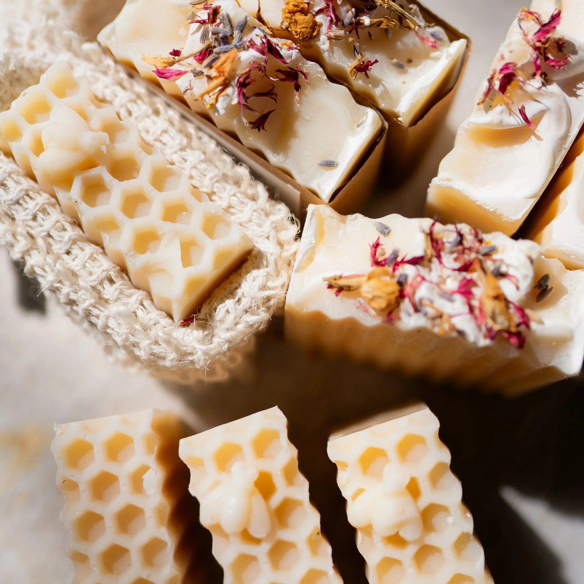 Close-up of handmade honey-colored honeycomb soap bars topped with dried flower petals, arranged on a neutral surface with a knitted soap dish.