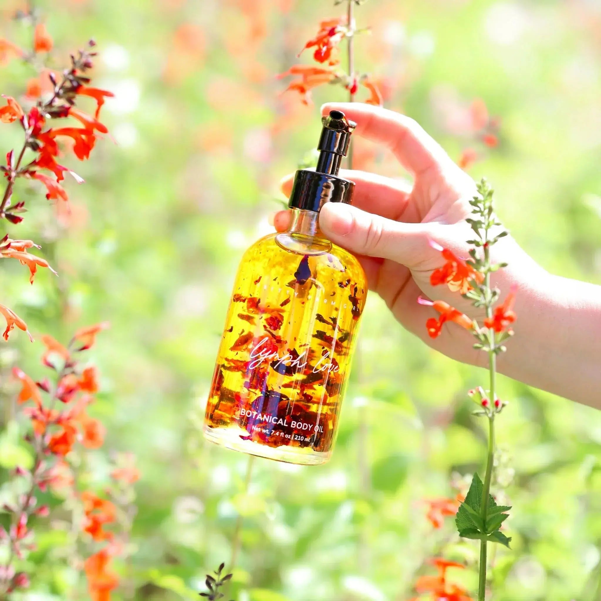 Hand holding botanical body oil with dried flowers, surrounded by orange blooms in garden setting