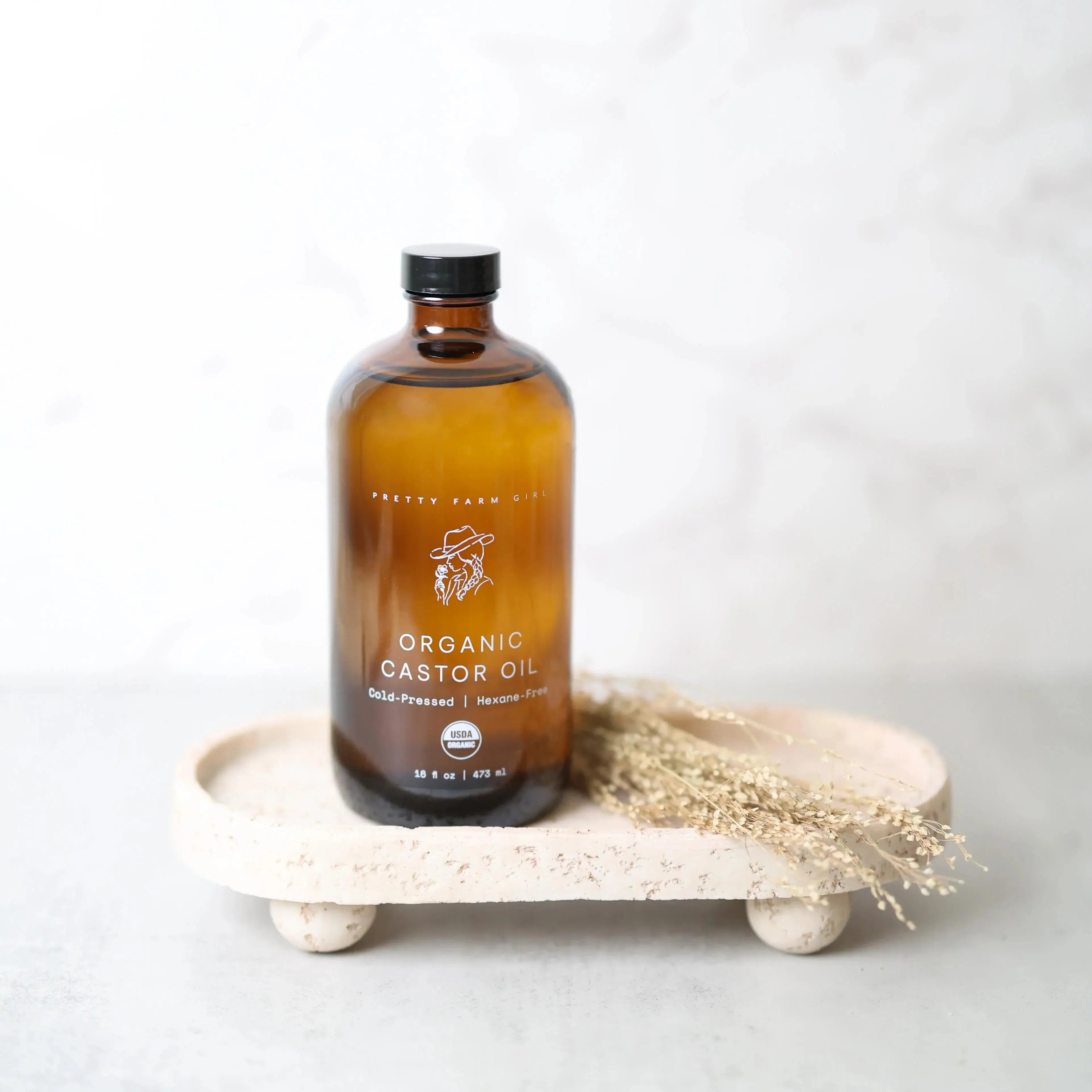 Organic castor oil in amber glass bottle with dried flowers on rustic tray, farmhouse decor