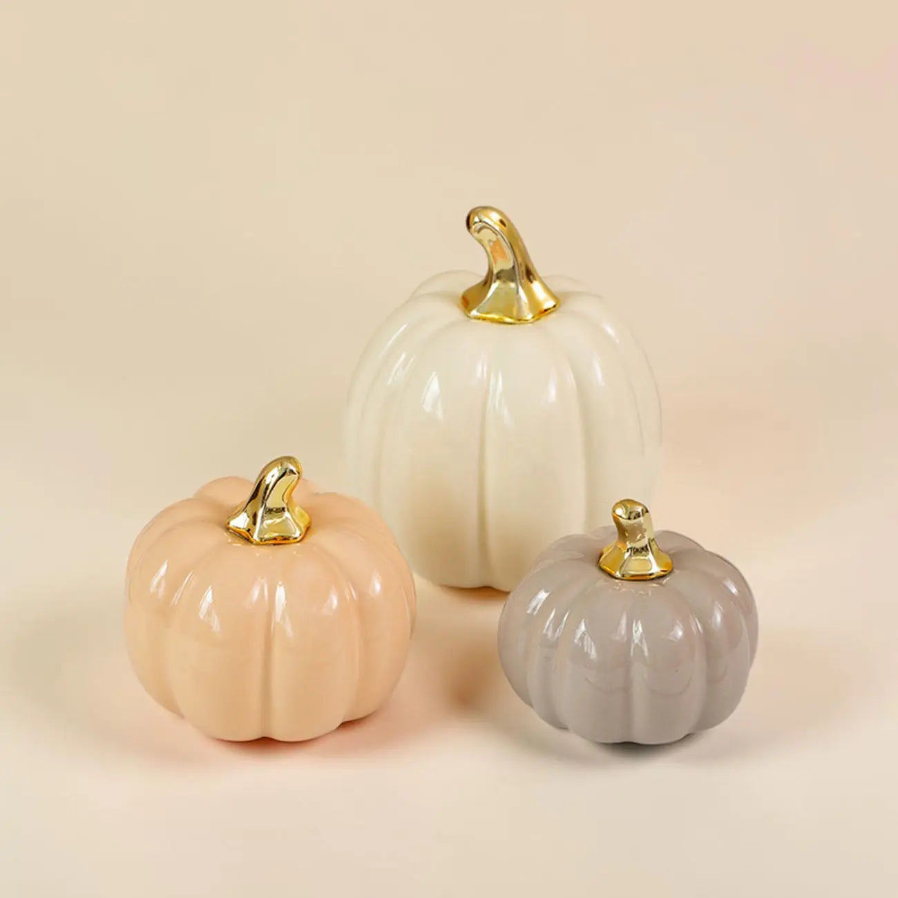Three decorative pumpkins in beige, white, and gray with gold stems on a beige background