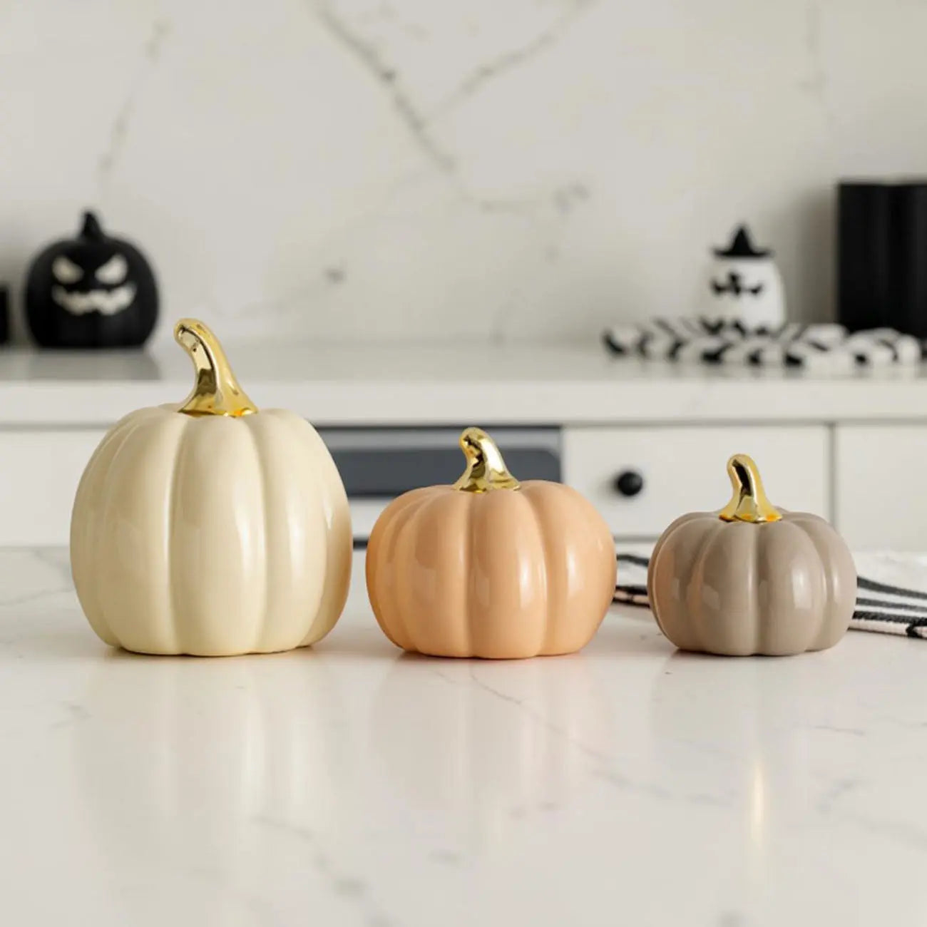 Three decorative pumpkins in gold, peach, and gray on a marble countertop.