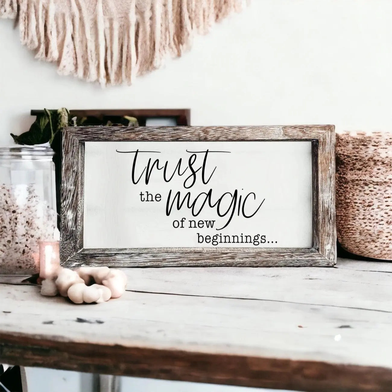 Framed sign with 'Trust the magic of new beginnings' text on a wooden surface.
