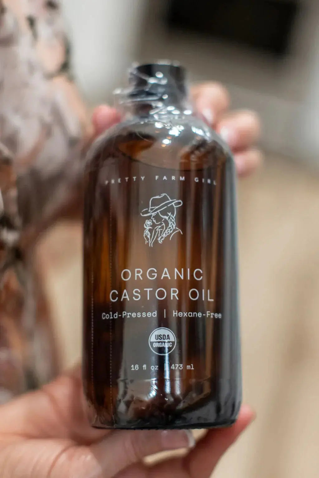 Organic castor oil in amber glass bottle, cold-pressed and USDA certified, held in hand for natural skincare