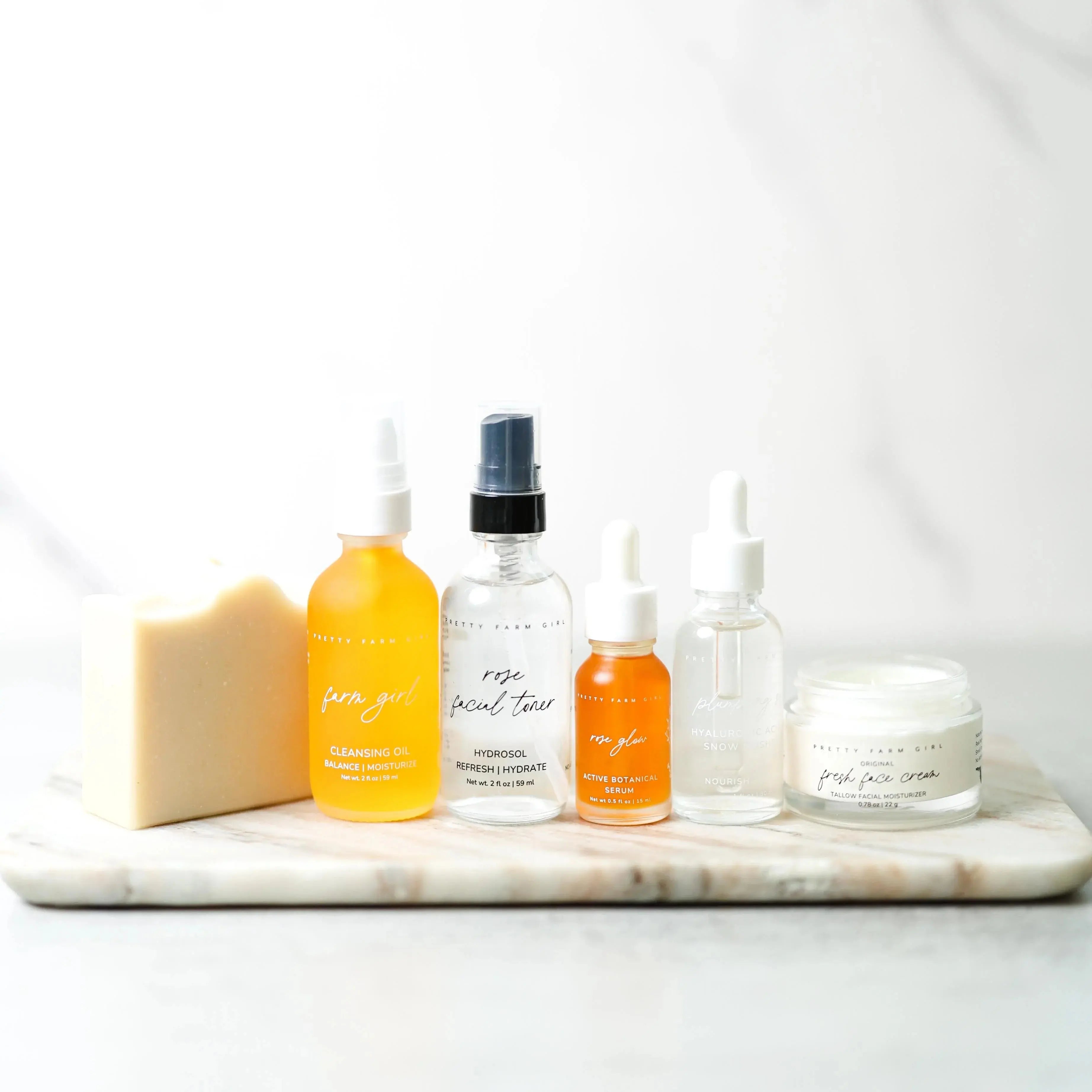 Farmhouse-style facial care set with cleansing oil, toner, serum, and moisturizer on marble tray