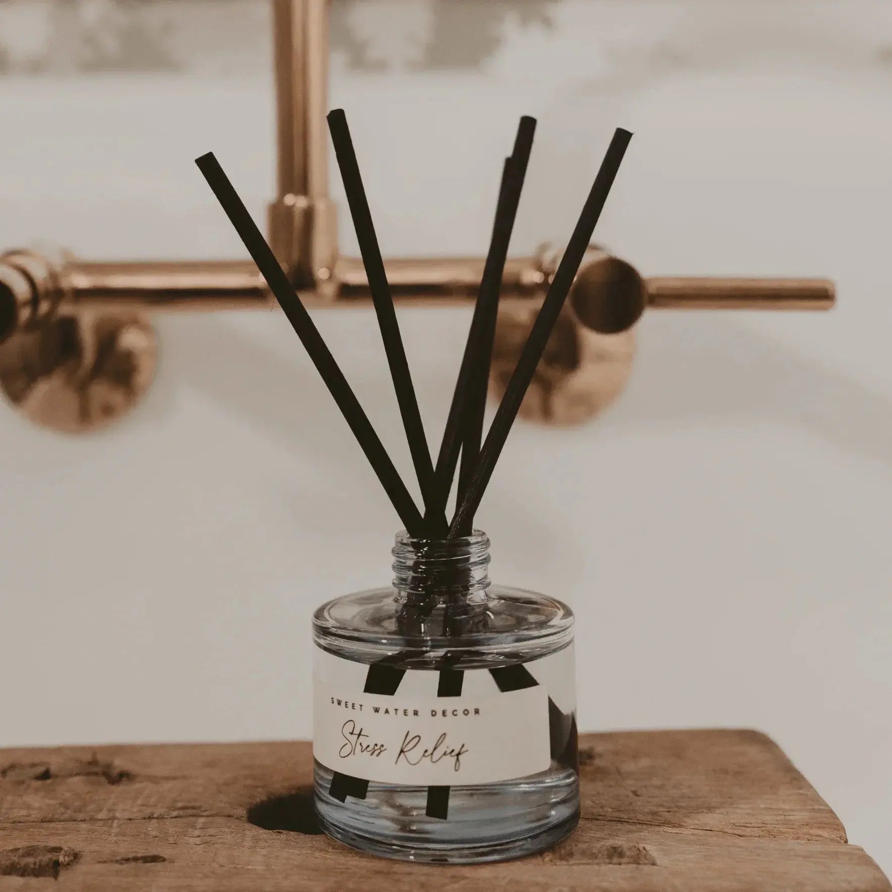 Stress Relief reed diffuser in clear glass bottle with black reeds, rustic wood surface, farmhouse bathroom decor