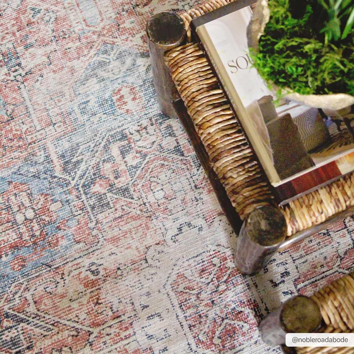 Vintage-style rug with red and blue patterns, styled with wicker tray, green moss, and decor for cozy farmhouse living spaces