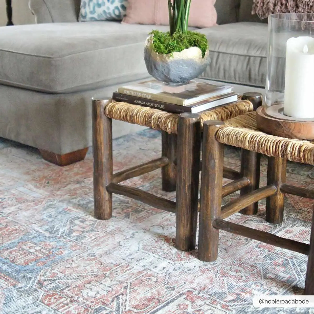 Rustic wooden side tables with woven tops, styled with books, moss planter, and candle for cozy farmhouse living room decor