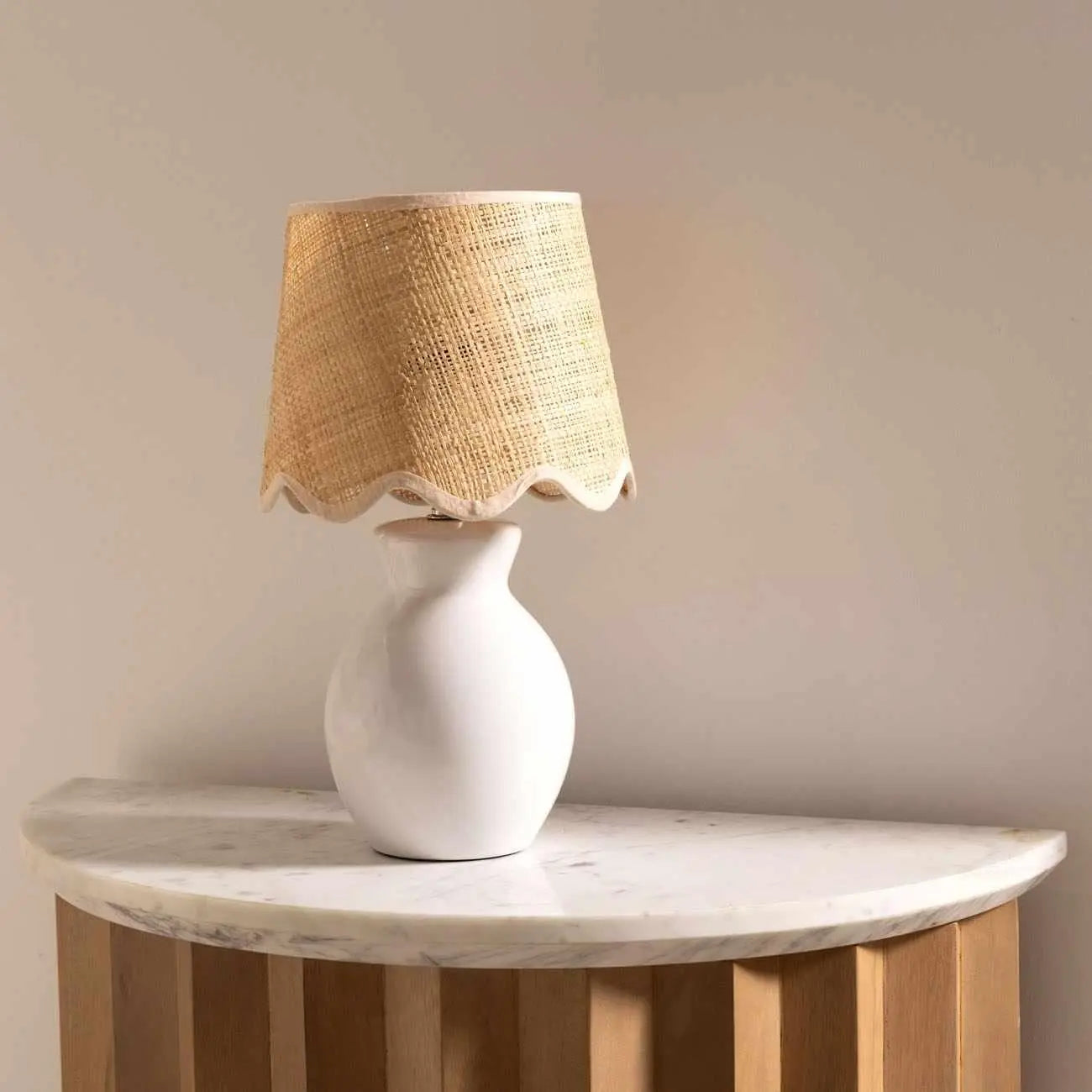 White ceramic table lamp with woven raffia shade on marble-top side table, farmhouse decor
