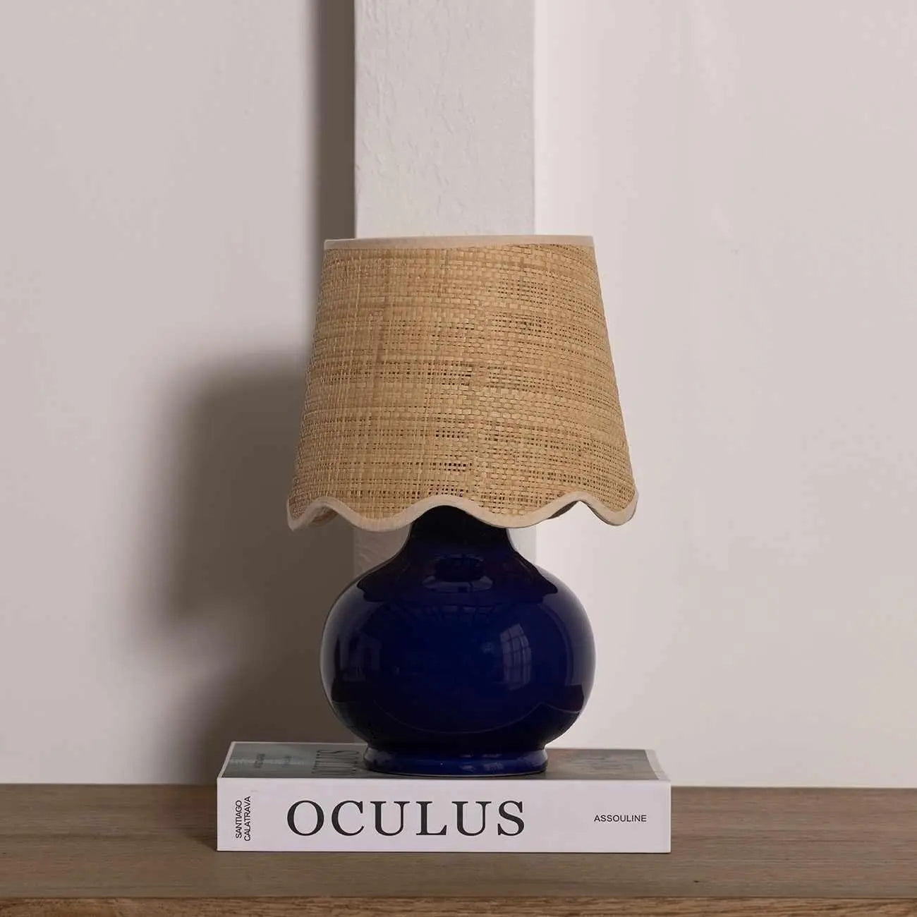 Navy blue ceramic table lamp with woven raffia shade, styled on book for cozy farmhouse decor