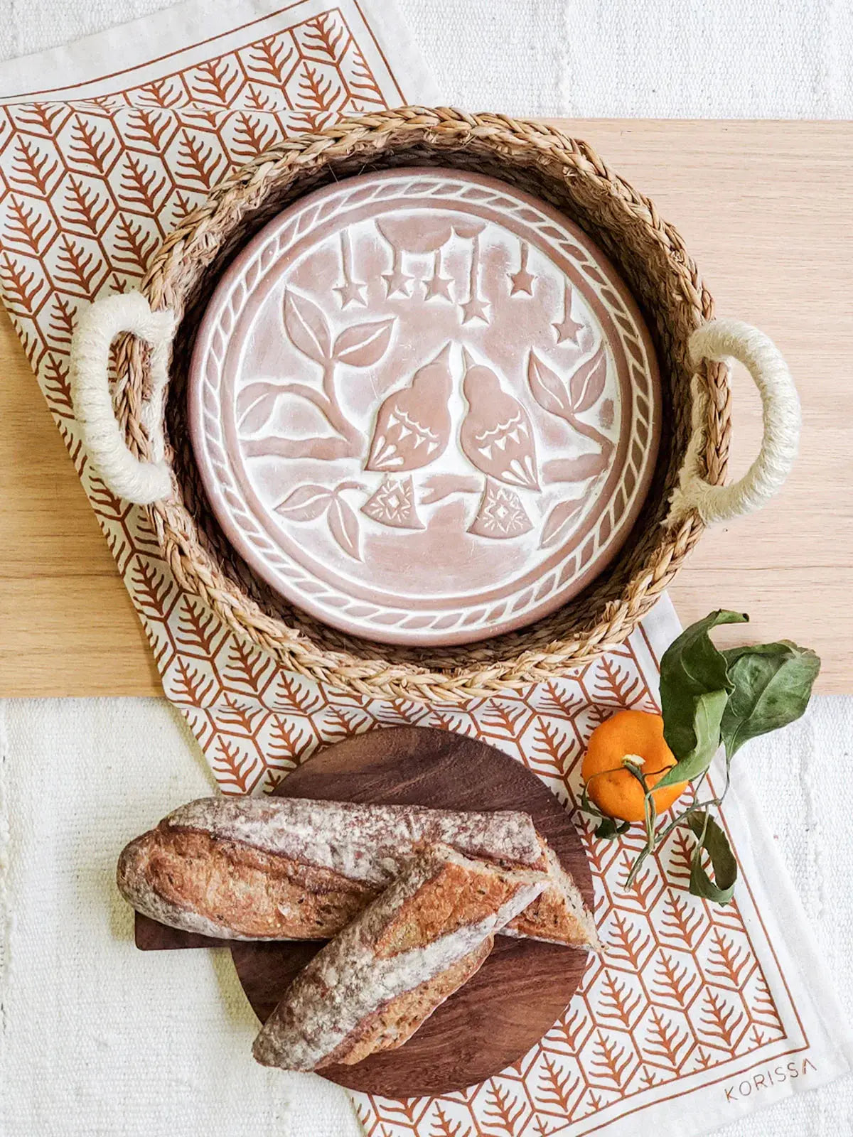 Farmhouse-style woven tray with embossed bird plate, rustic bread, and orange on patterned napkin