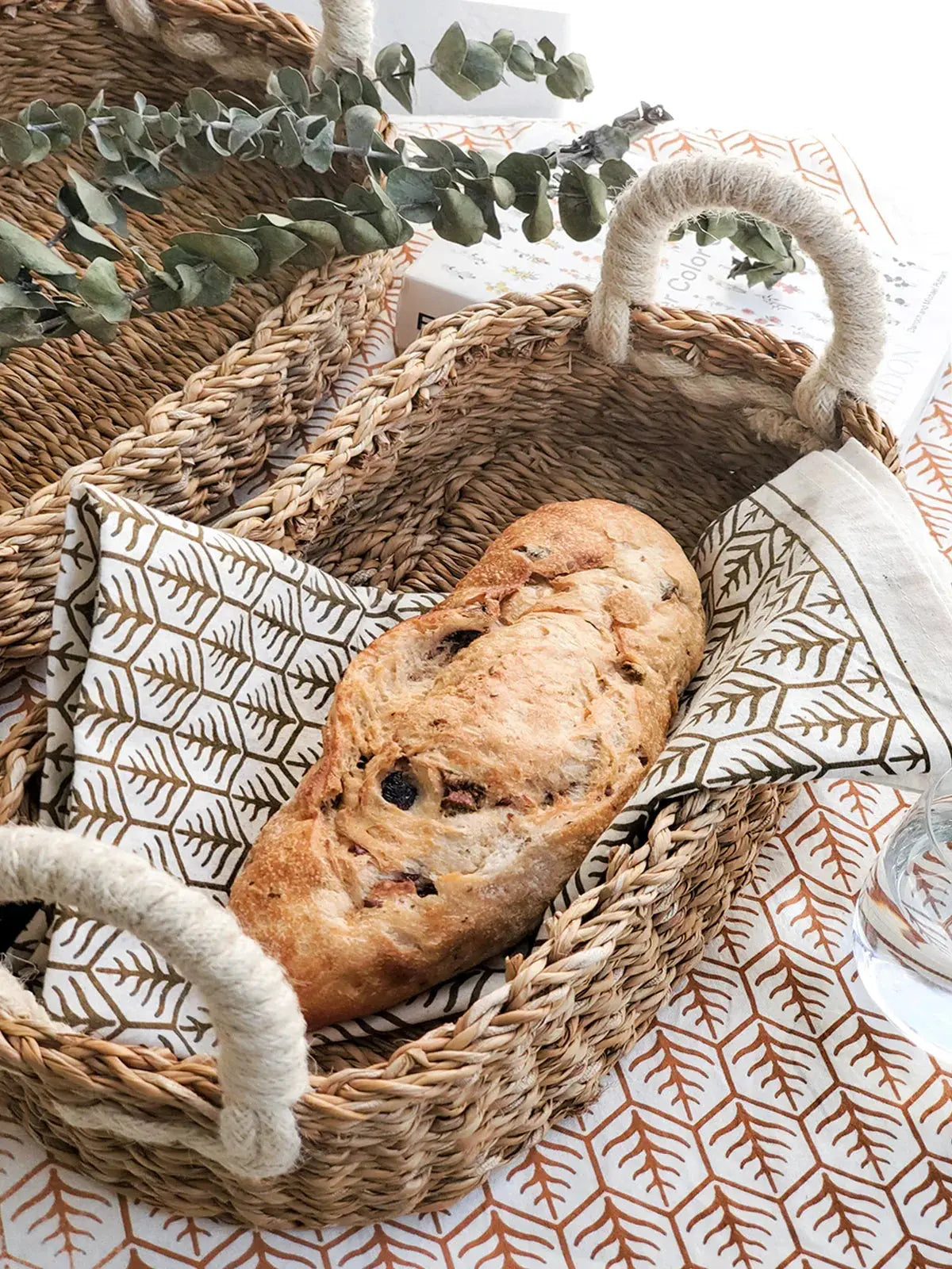 Rustic woven basket with fresh bread, eucalyptus, and leaf-patterned napkin for cozy farmhouse table decor