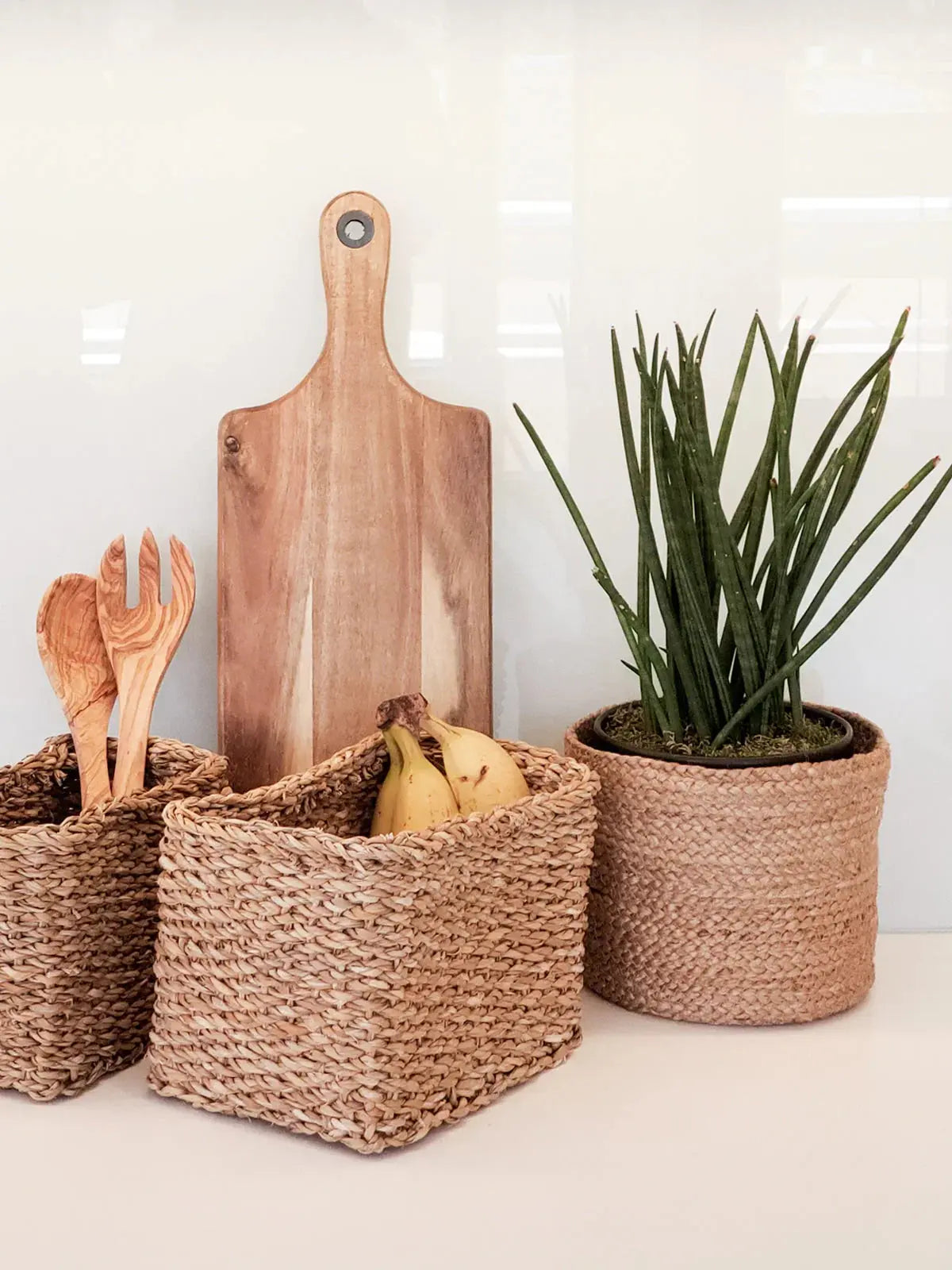 Woven seagrass baskets with wooden utensils, cutting board, bananas, and potted plant for cozy farmhouse kitchen decor
