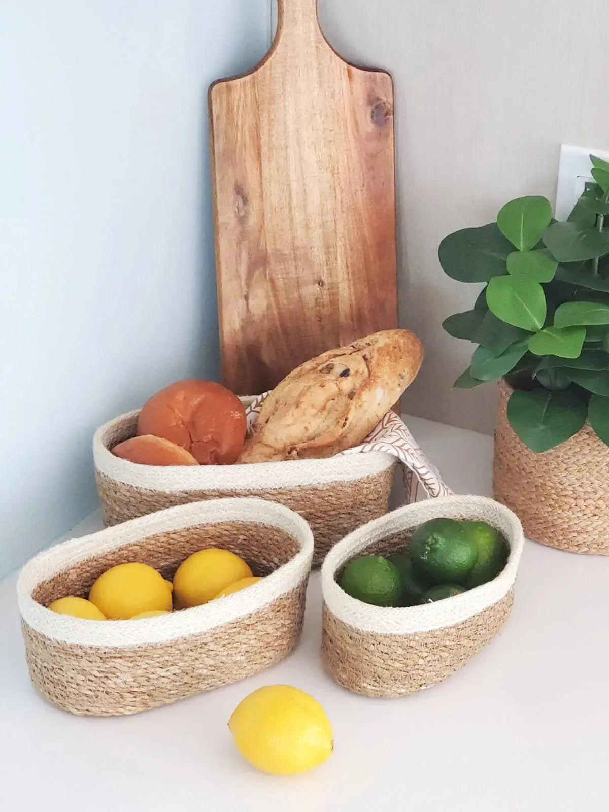 Woven seagrass baskets with lemons, limes, and bread, styled with wooden cutting board and green plant for farmhouse kitchen decor